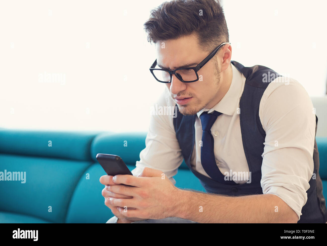 Businessman sitting on couch lunettes avec le smartphone à bouleversé et confus Banque D'Images