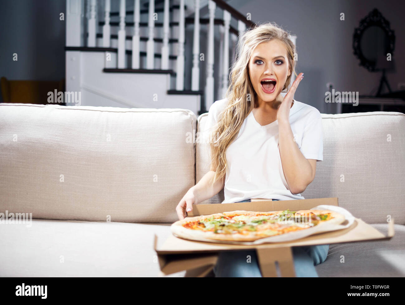 Surpris woman eating pizza et regarder sur canapé au salon Banque D'Images
