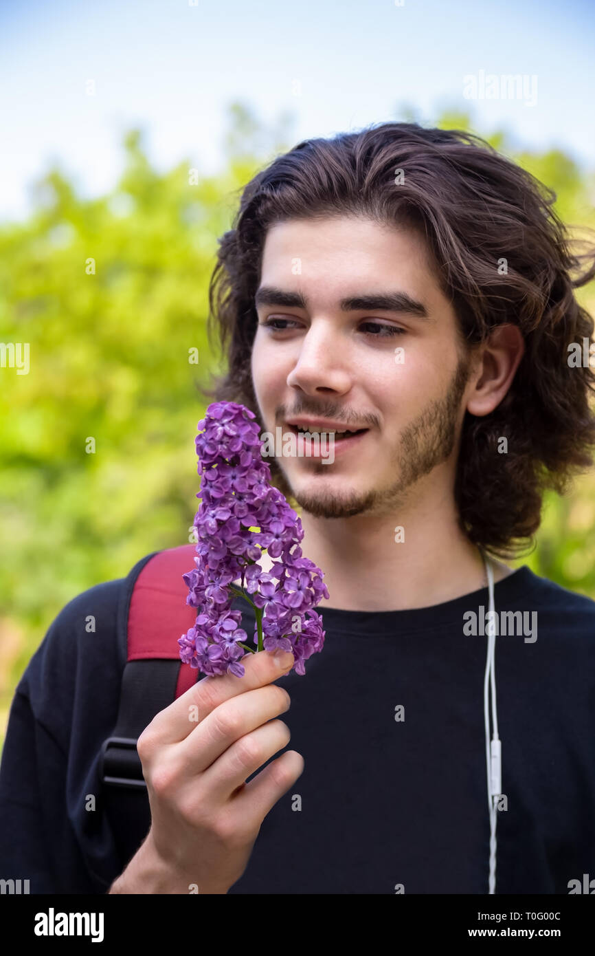 Jeune brunette guy l'odeur des fleurs fraîches sur la branche de lilas et regarde ailleurs et sur un arrière-plan flou. Banque D'Images