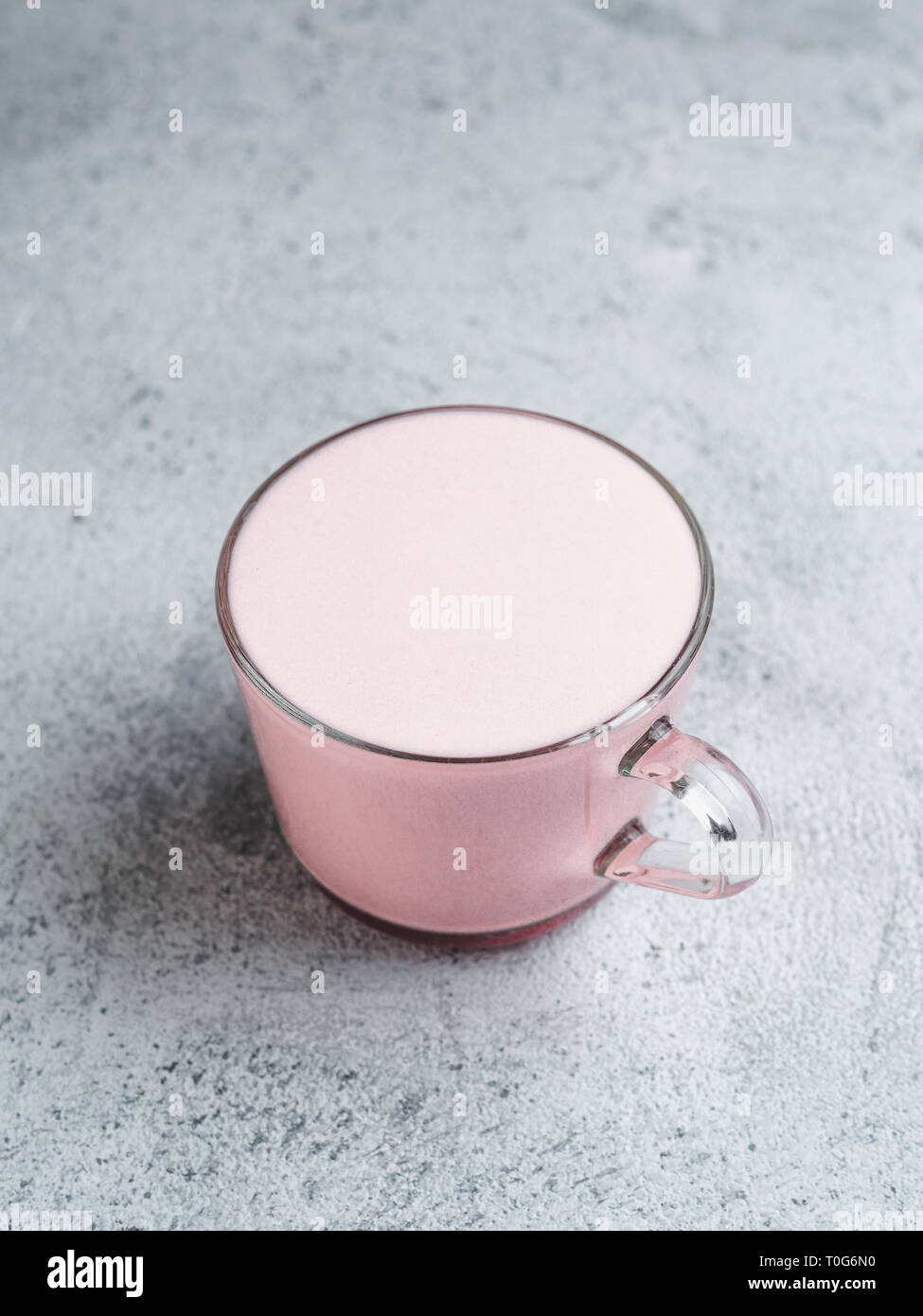 Boisson à la mode : pink latte. Betterave rouge ou framboise cappuccino ou latte dans verre tasse sur fond de ciment gris. L'espace de copie pour le texte. La verticale. Banque D'Images