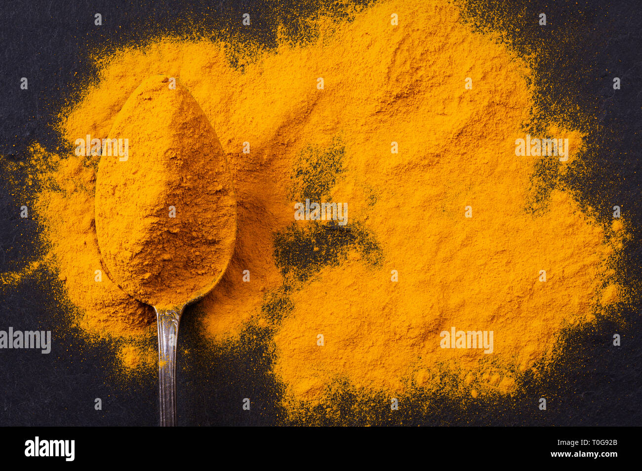 Des tas d'épices curcuma curcuma avec cuillère sur fond ardoise noir foncé, vue du dessus Banque D'Images