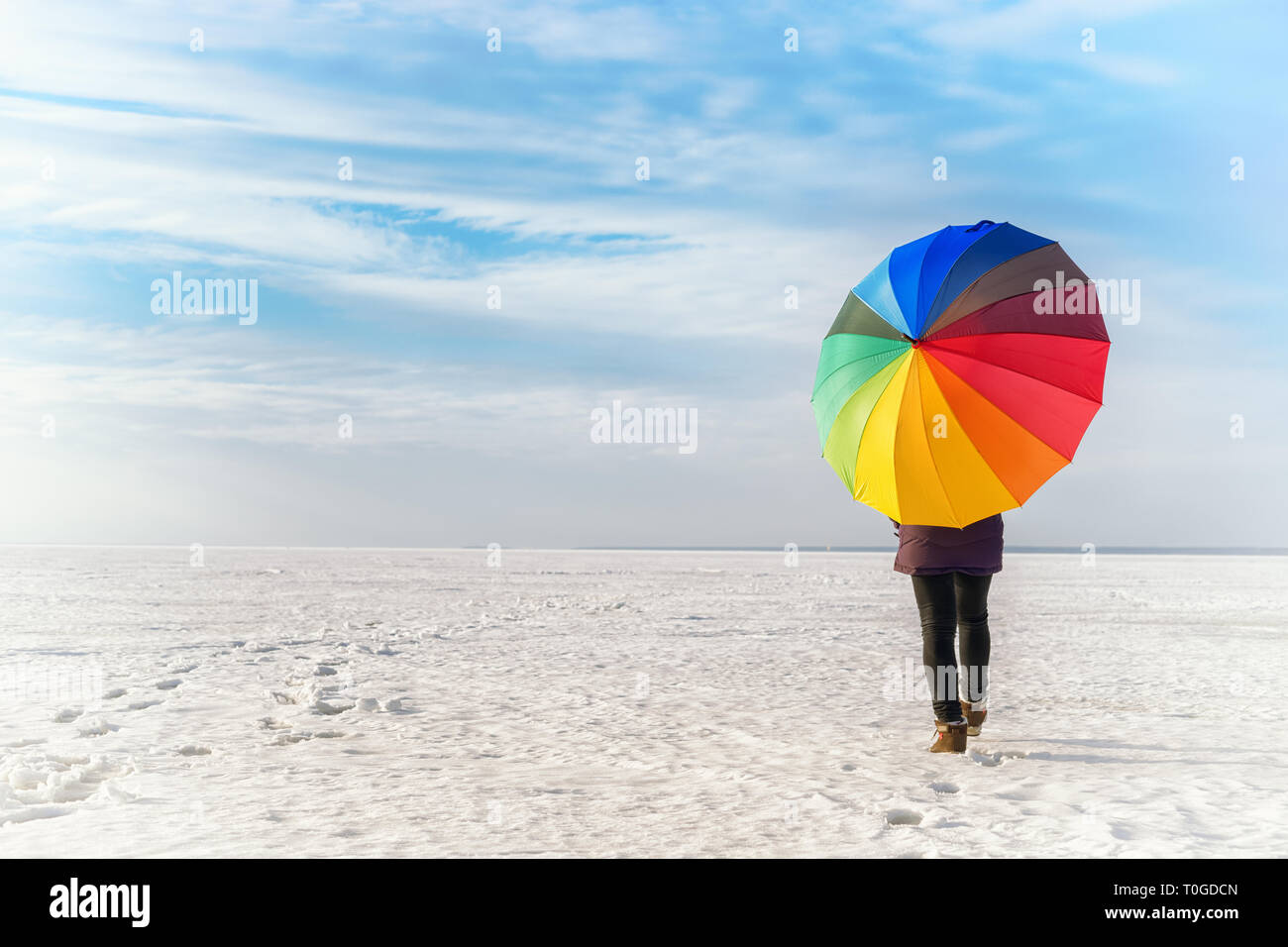 Femme avec parapluie de couleur arc-en-ciel en marchant sur la mer gelée. Paysage d'hiver de couleur vive Banque D'Images