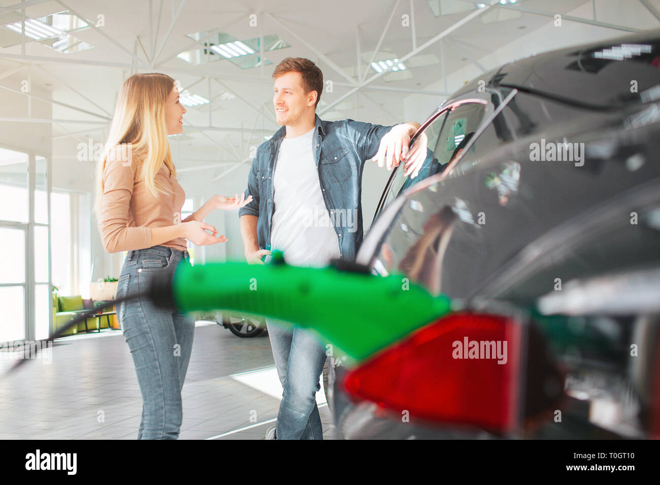 Jeune couple qui achète une première voiture électrique dans une salle d'exposition. Concept de véhicule écologique. La technologie moderne dans l'industrie automobile Banque D'Images