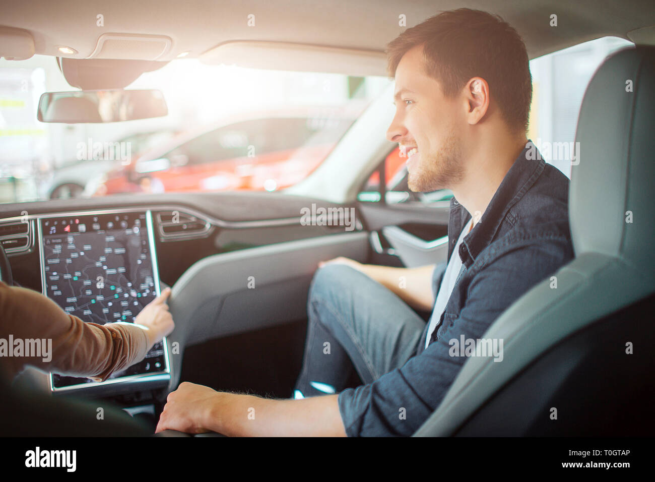 Jeune couple l'achat première voiture électrique dans la salle de spectacle. Heureux l'homme regardant attrayant sa petite amie pendant qu'elle chooising un moyen sur le Banque D'Images