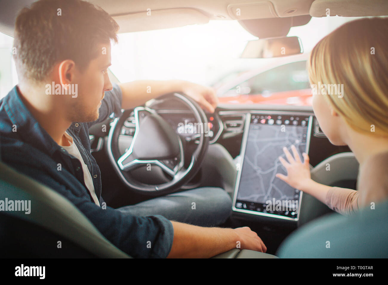 Jeune famille l'achat première voiture électrique dans la salle de spectacle. Beau couple chooising un moyen sur le tableau de bord de véhicule hybride électrique moderne Banque D'Images