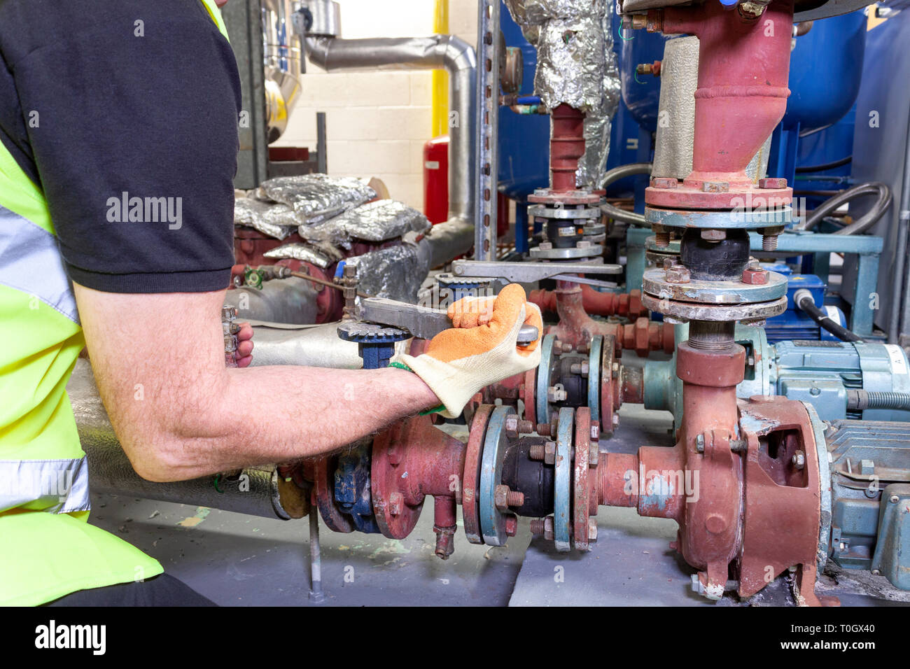 Ingénieur mécanique dans un gilet de sécurité haute visibilité travaille sur un ensemble de pompe dans une chaufferie Banque D'Images