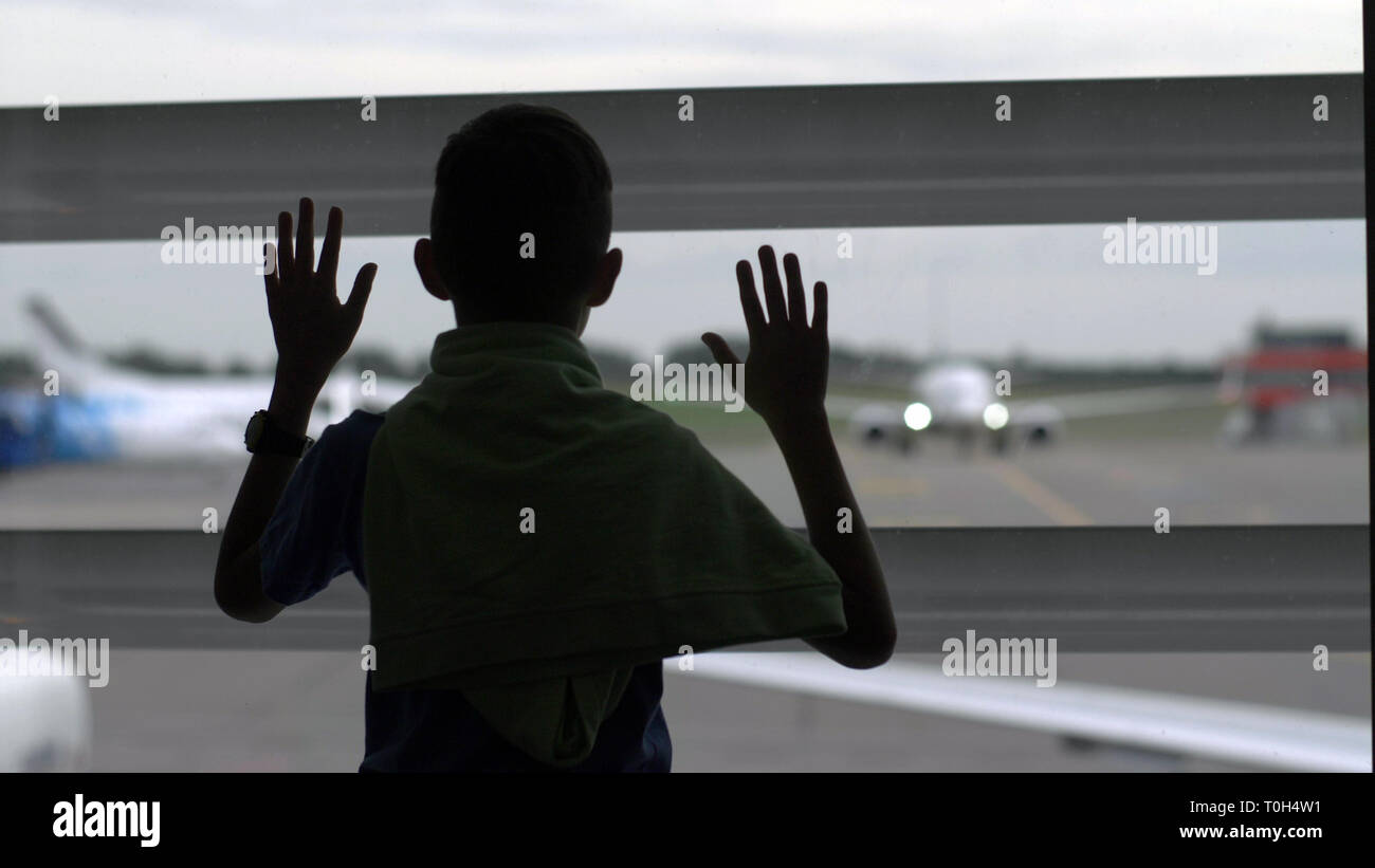 Boy stands près de la fenêtre à l'aéroport et il s'intéresse aux avions, le garçon rêve de devenir un pilote, s'amuser Banque D'Images