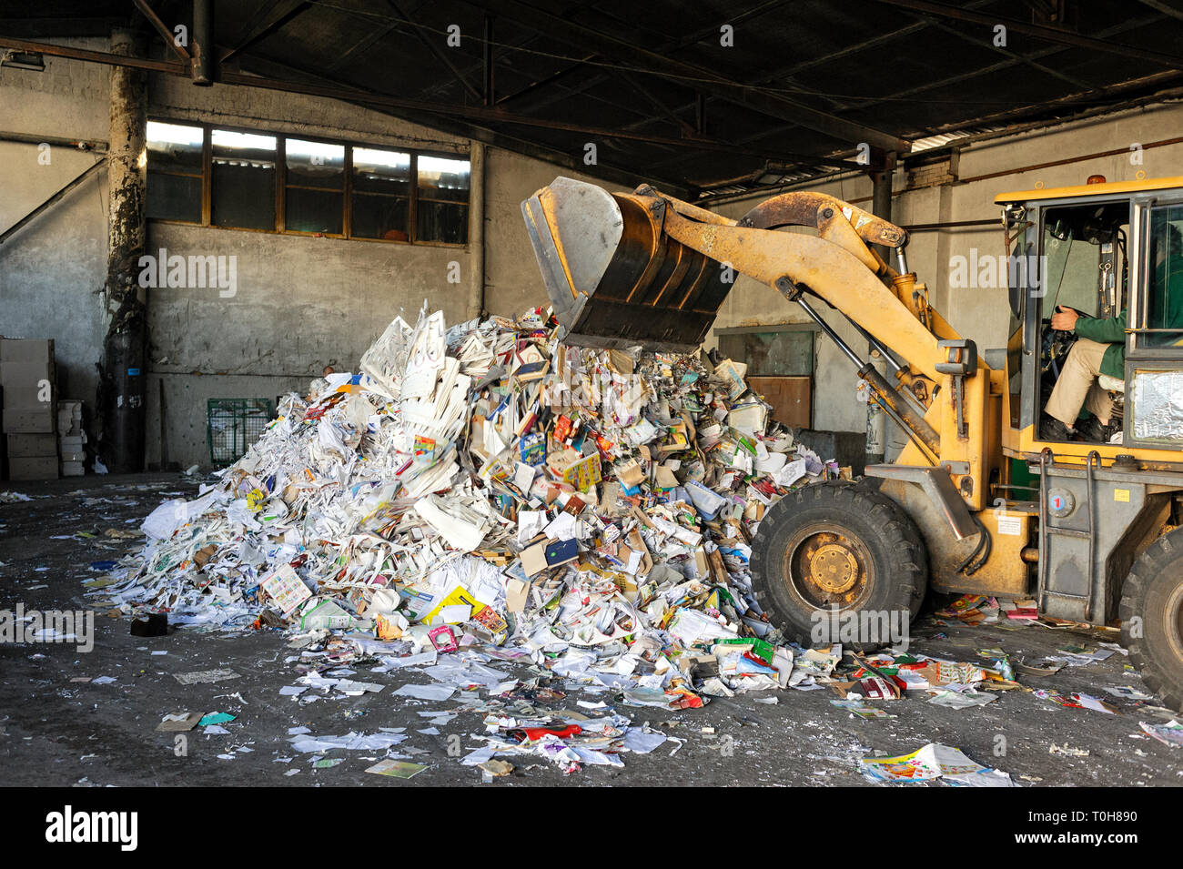 Excavatrice jaune déverse des centaines d'articles et ouvrages. À l'usine de recyclage du papier de l'excavateur lance Corbeille. Kiev, Ukraine, l'usine Kyivmyskvtorresursy (K Banque D'Images