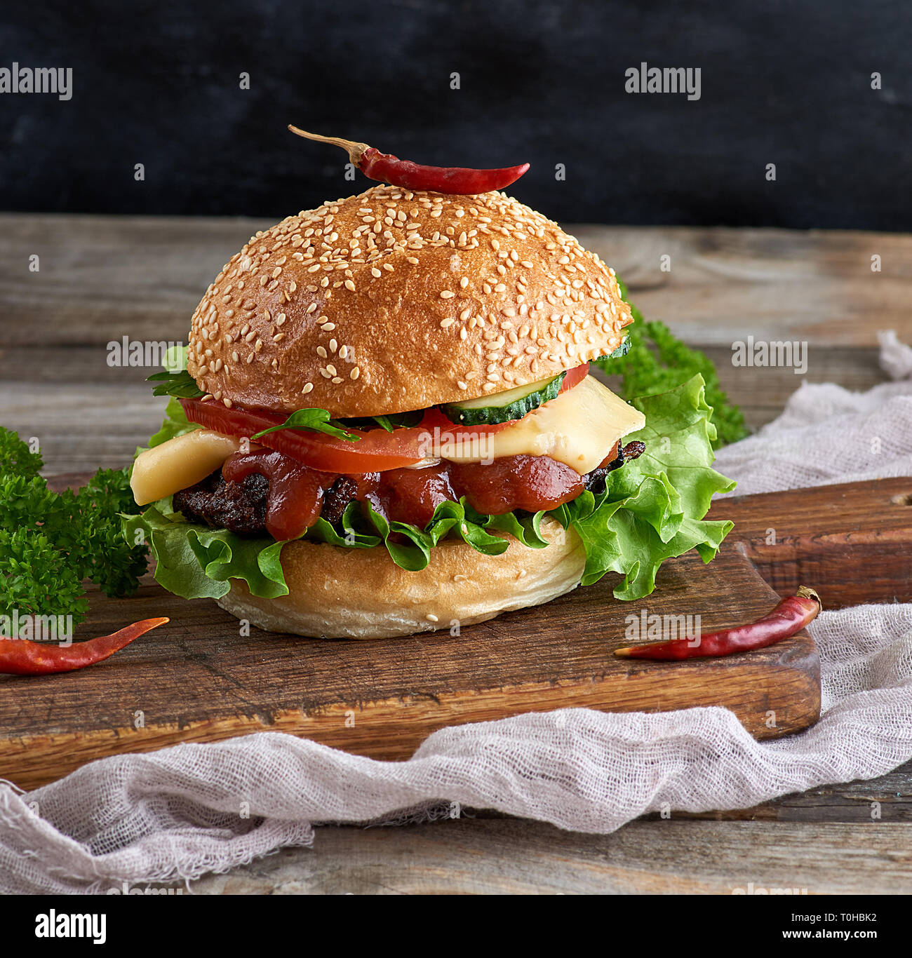 Burger maison avec de la laitue, le fromage, l'oignon et la tomate sur une planche de bois rustique, Close up Banque D'Images