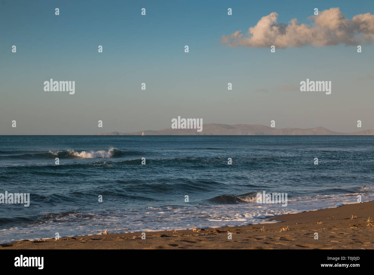 La fin de l'afteroon à la plage. Sable doré, l'eau d'un bleu profond de la mer Méditerranée avec de petites vagues. Montagne sur l'horizon. Ciel bleu avec un gros nuage Banque D'Images