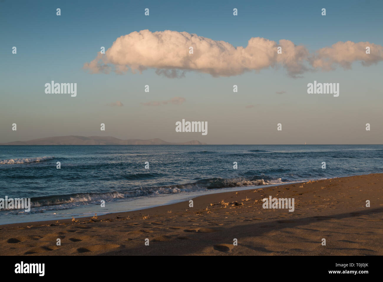 La fin de l'afteroon à la plage. Sable doré, l'eau d'un bleu profond de la mer Méditerranée avec de petites vagues. Montagne sur l'horizon. Ciel bleu avec un gros nuage Banque D'Images