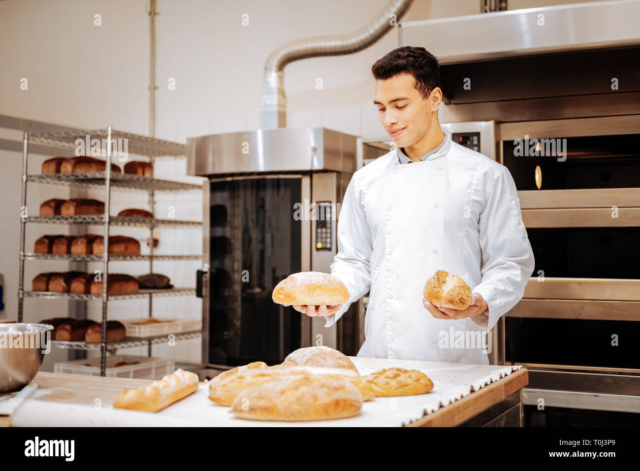 Dark-haired satisfait baker tenant deux loafs de pain dans ses mains Banque D'Images