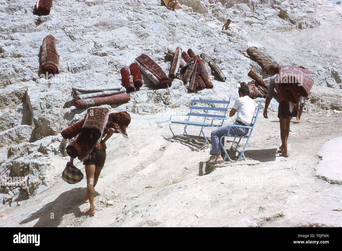 Les gens portent des tapis orientaux à travers un désert mise en préparation pour laver le tapis dans une oasis en Iran, août 1971. () Banque D'Images