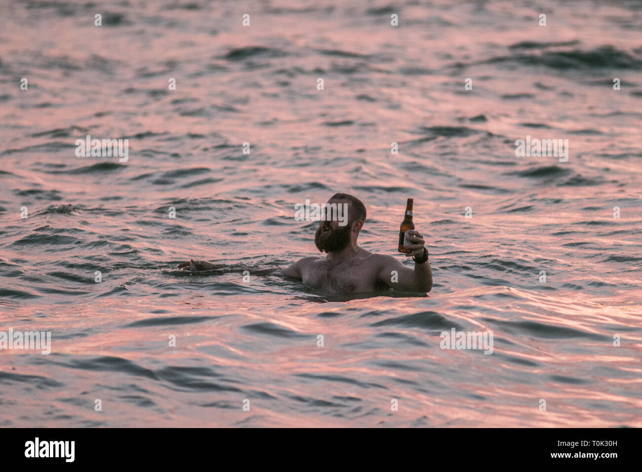 Adélaïde, Australie. Mar 21, 2019. Les nageurs dans les eaux de l'océan porter un toast avec des bouteilles de bière comme le coucher de soleil sur plage de Grange à Adélaïde : Crédit amer ghazzal/Alamy Live News Banque D'Images