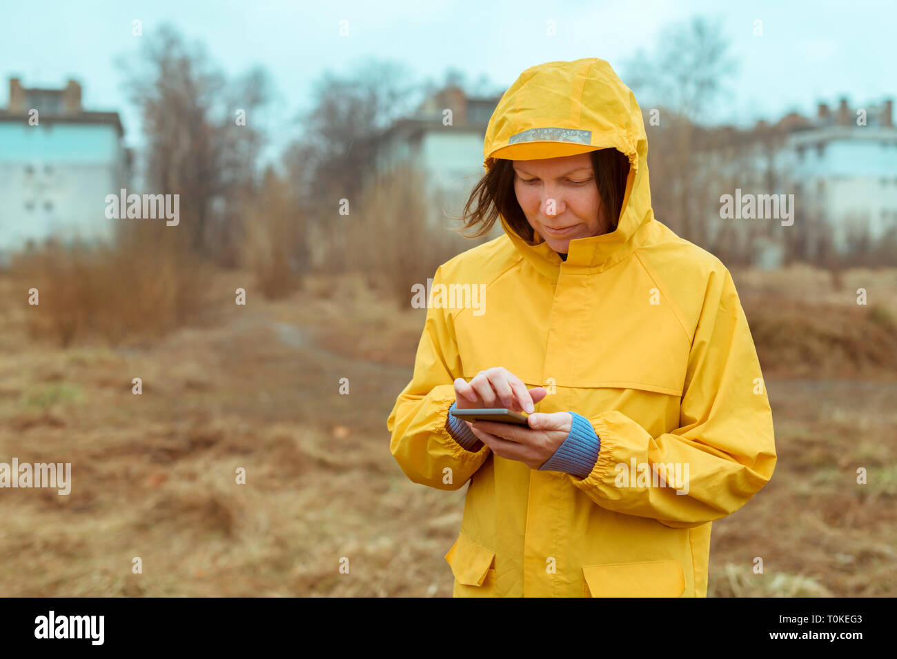 Femme en imperméable jaune sms sur téléphone mobile à l'extérieur sur jour de pluie Banque D'Images