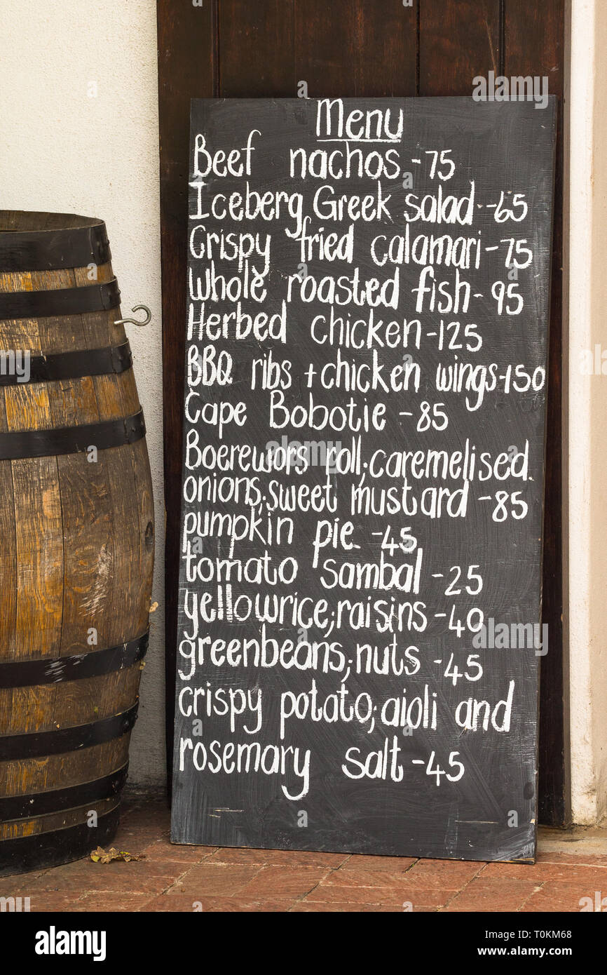 Restaurant menu écrit sur un tableau noir appuyé contre une surface en plein air à côté d'un baril de vin sud-africains de la nourriture et les repas à Cape Winelands Banque D'Images