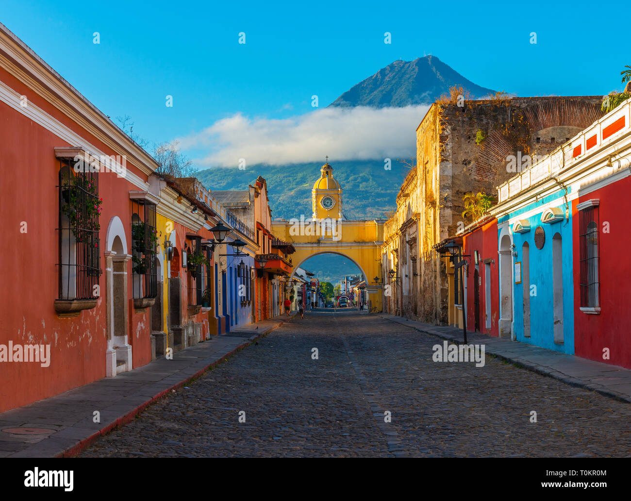 Paysage urbain de la rue principale et jaune Santa Catalina arch dans le centre-ville historique d'Antigua au lever du soleil avec le volcan Agua, au Guatemala. Banque D'Images