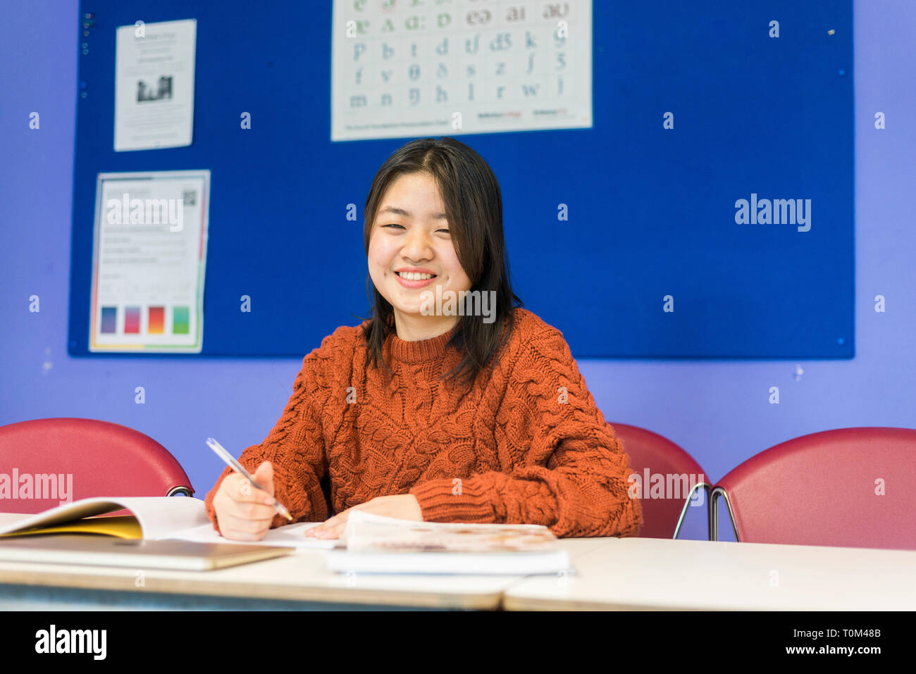 Un jeune étudiant asiatique est assis à un bureau dans une salle de classe à étudier au cours de sa leçon. Banque D'Images