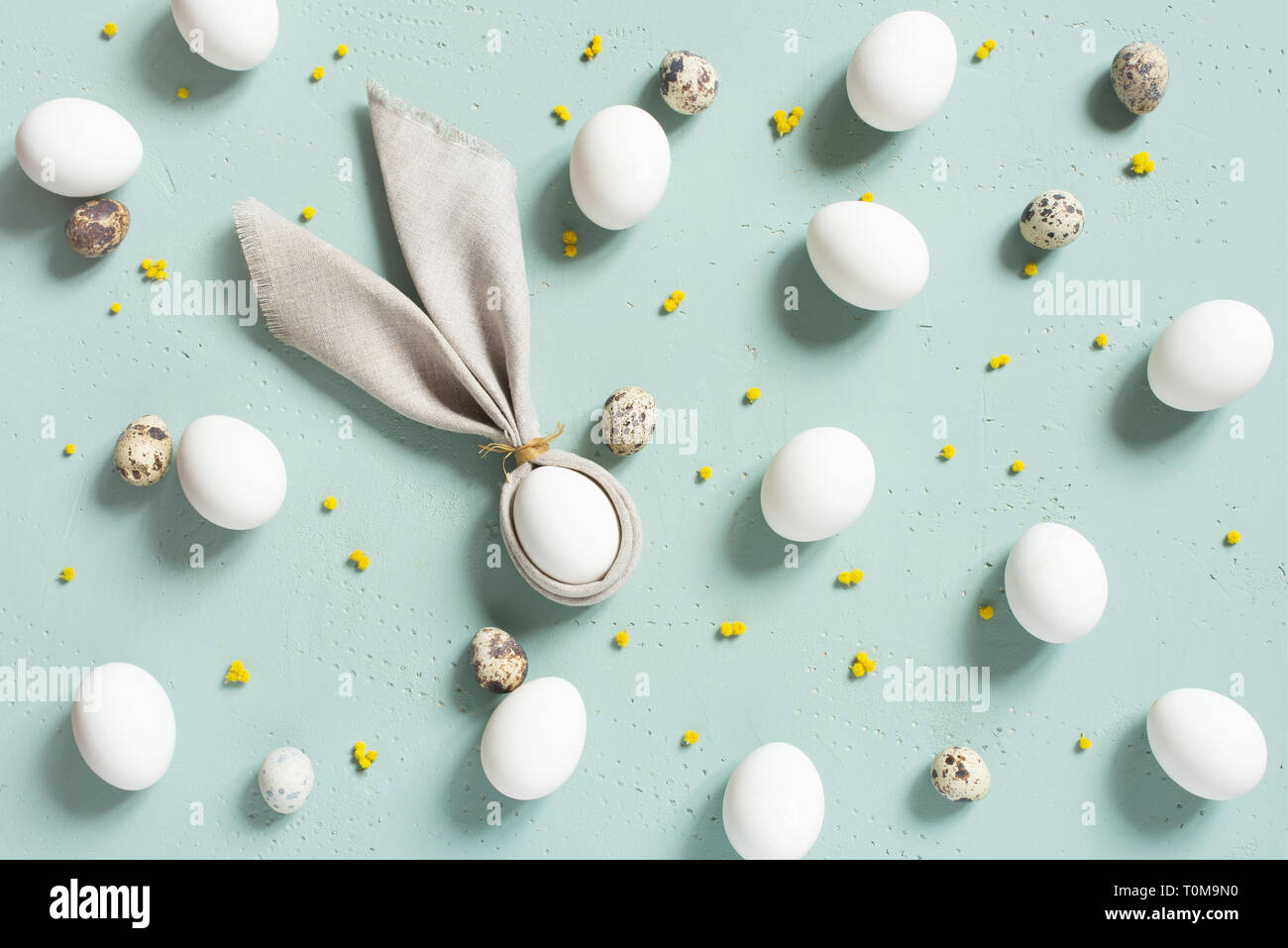 Modèle de poulet et des oeufs de cailles avec oreilles de lapin de draps, serviette de petites fleurs jaunes sur la table, texturé bleu composition Pâques, vue du dessus Banque D'Images