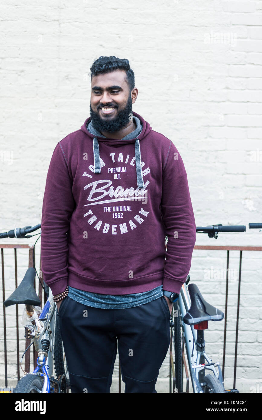 Un male international étudiant asiatique du sous continent, se dresse au milieu de la moto / stockage cycle dans un collège de Cambridge Banque D'Images