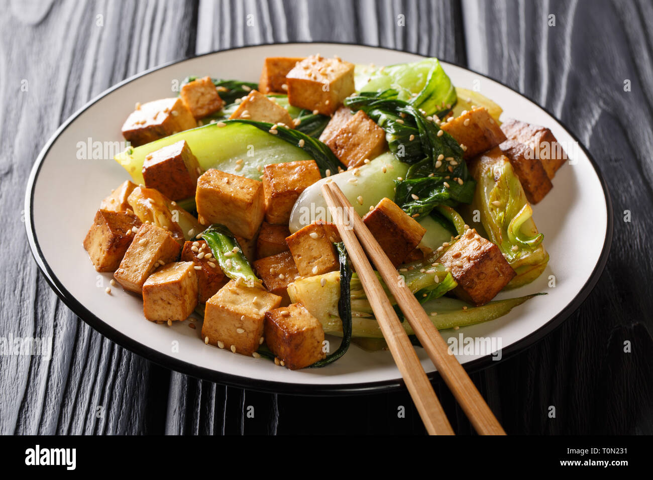 Dietary sauté de tofu avec petits bok choy, la sauce soja et les graines de sésame gros plan sur une assiette sur la table horizontale. Banque D'Images