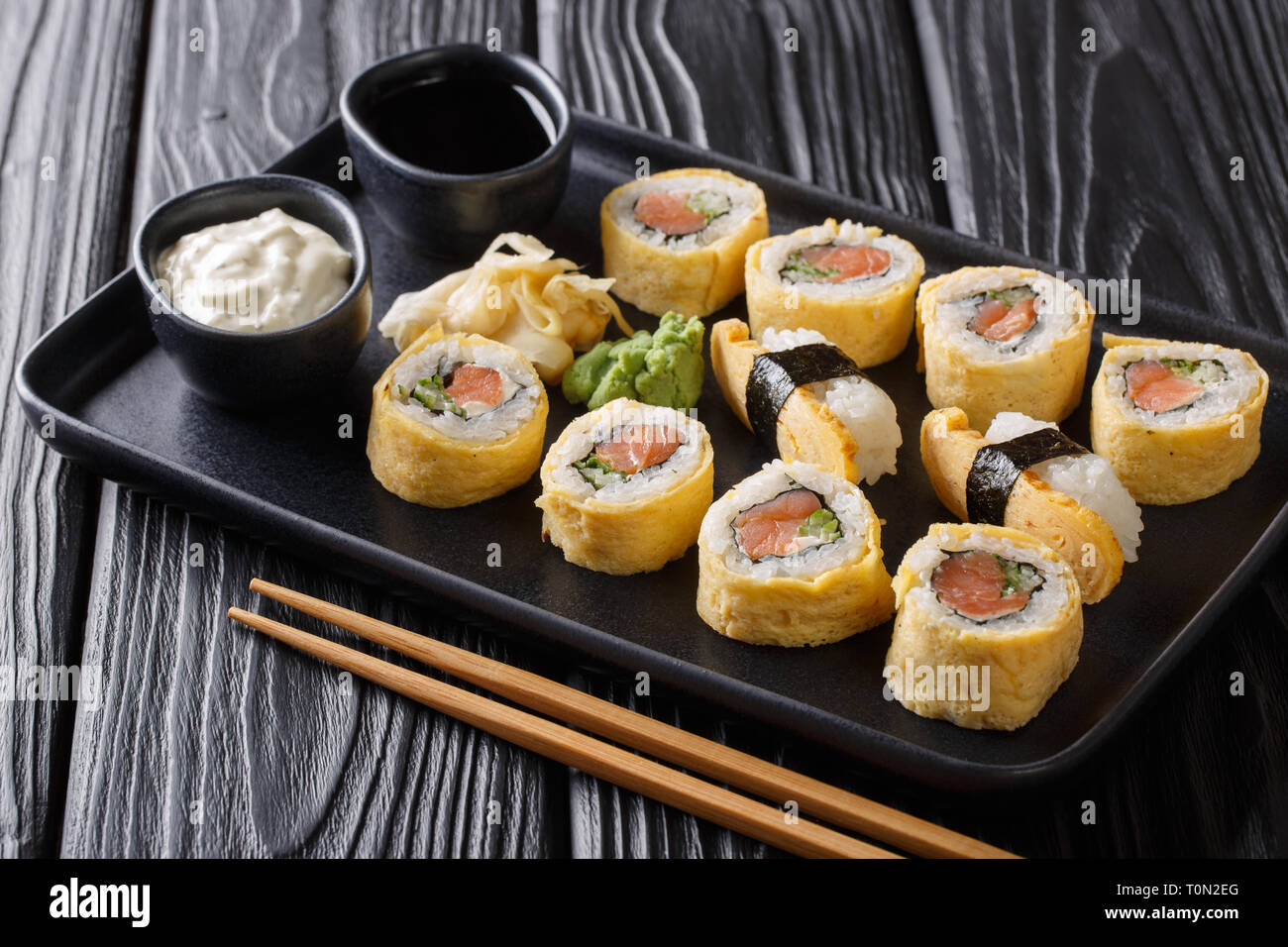 Omelette Tamagoyaki set rouleaux de sushi avec du riz, du saumon fumé et d'avocat close-up avec des sauces, le wasabi et le gingembre sur une plaque sur un tableau noir. horizont Banque D'Images
