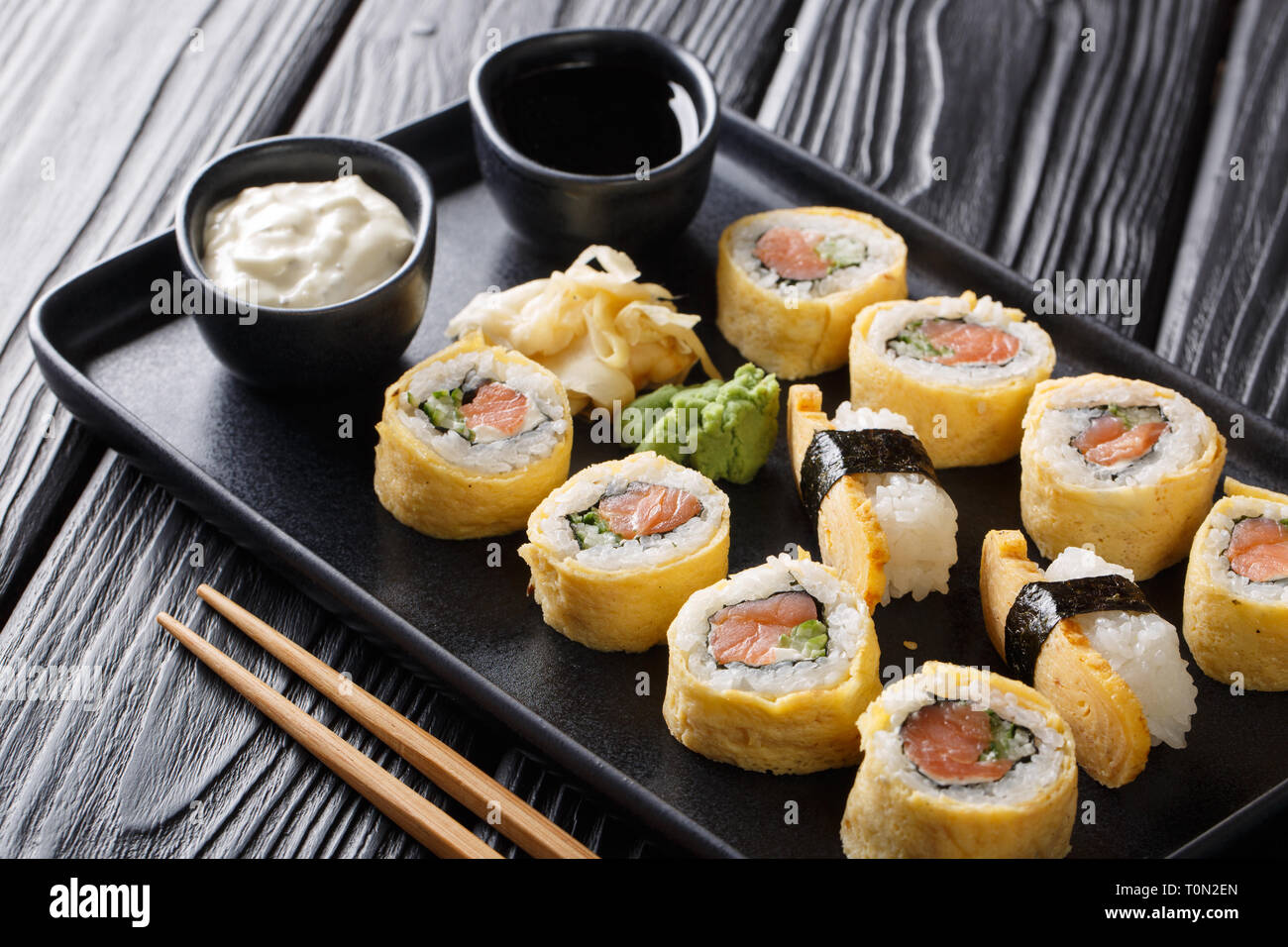 Tamagoyaki set sushi roll avec du riz, de l'omelette, du fromage, du saumon et d'avocat servi avec des sauces, le wasabi et le gingembre sur une plaque sur la table horizontale. Banque D'Images