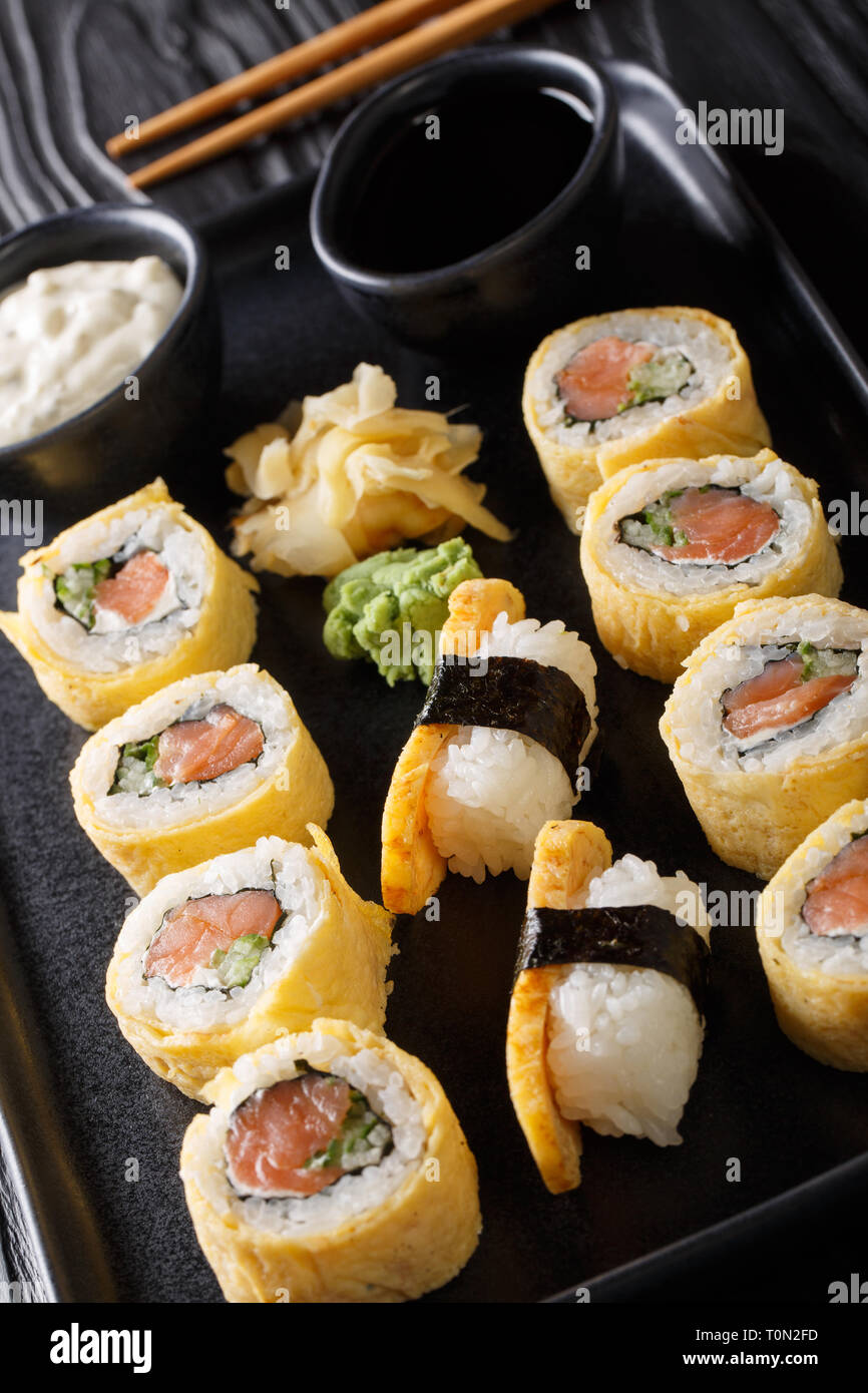 Tamagoyaki sushi roll avec du riz, du fromage, du saumon et d'avocat libre sur une plaque verticale sur la table. Banque D'Images