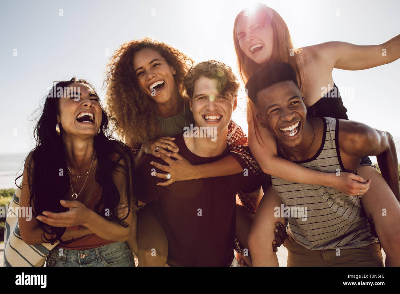Carefree jeunes amis profiter de week-end ensemble à l'extérieur. Hommes portant les femmes dans leur dos et de rire. Banque D'Images