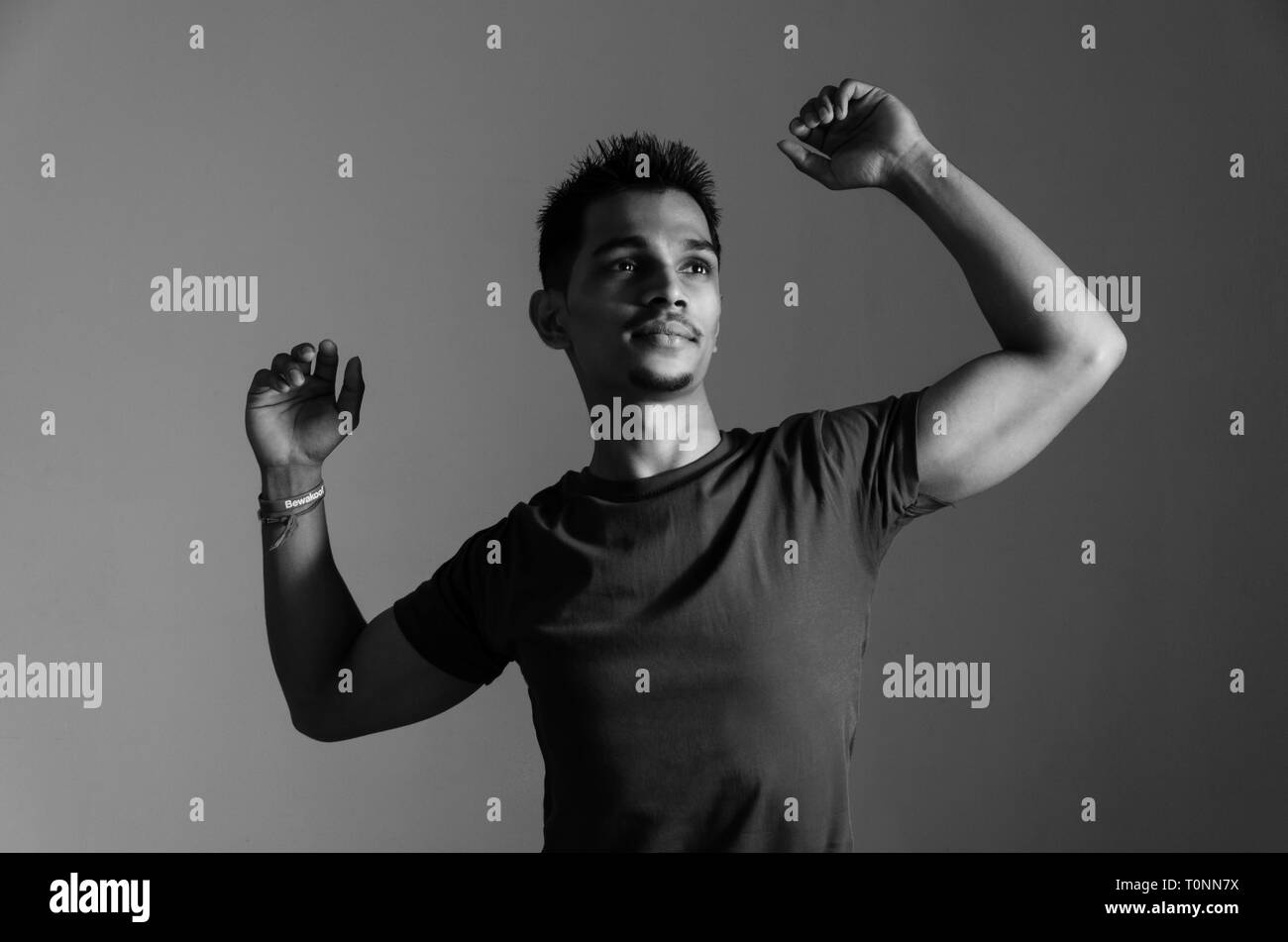 Le noir et blanc, portrait d'un jeune Indien de 22 ans montrant les mains tout en vous relaxant musculaire et à l'écart de caméra sur un arrière-plan uni, blanc. Banque D'Images