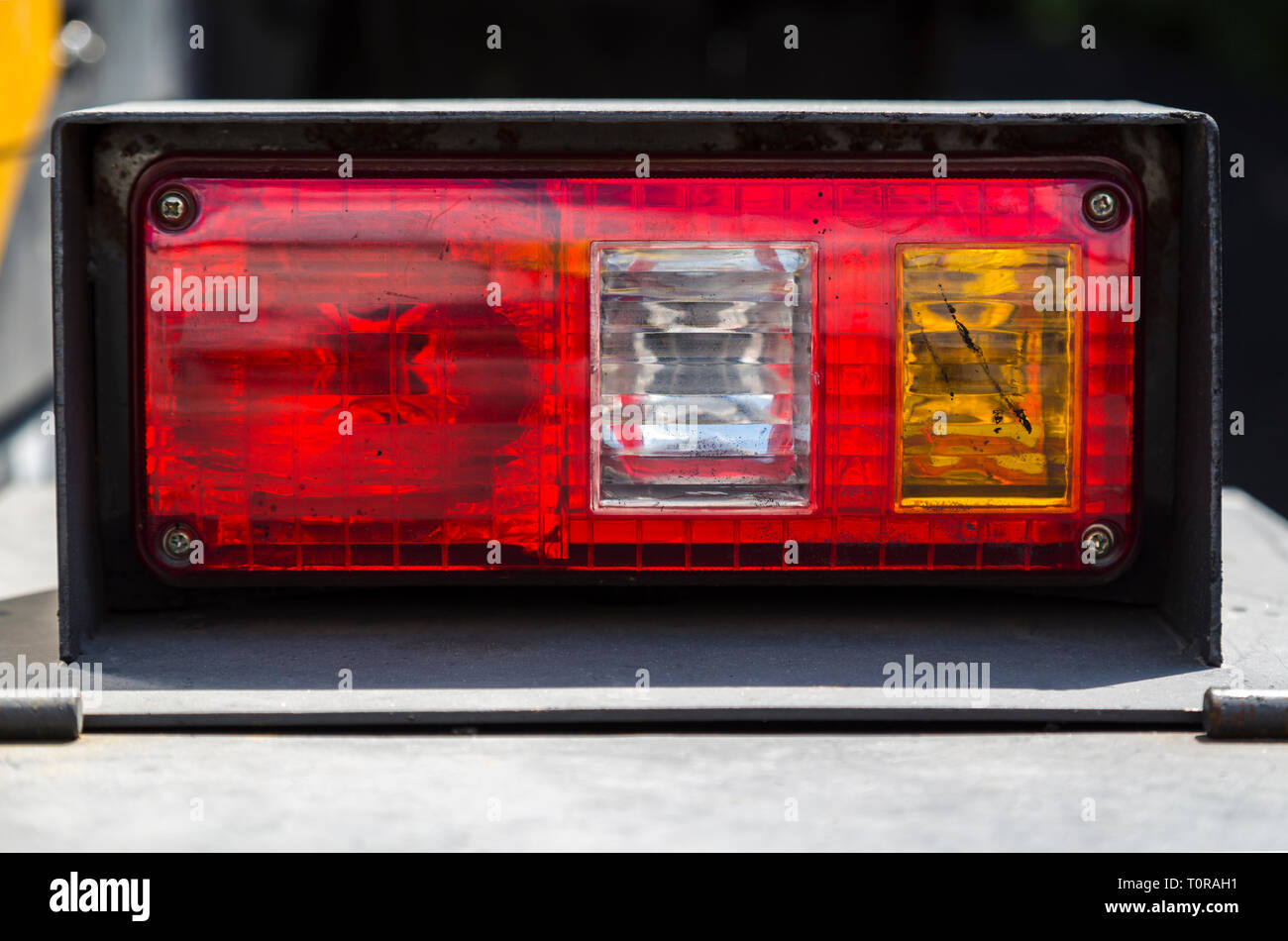 Phare rouge blanc et jaune avec des lampes, des taches de bitume, sur une route poussiéreuse corps de machines, gros plan sur un fond sombre floue Banque D'Images