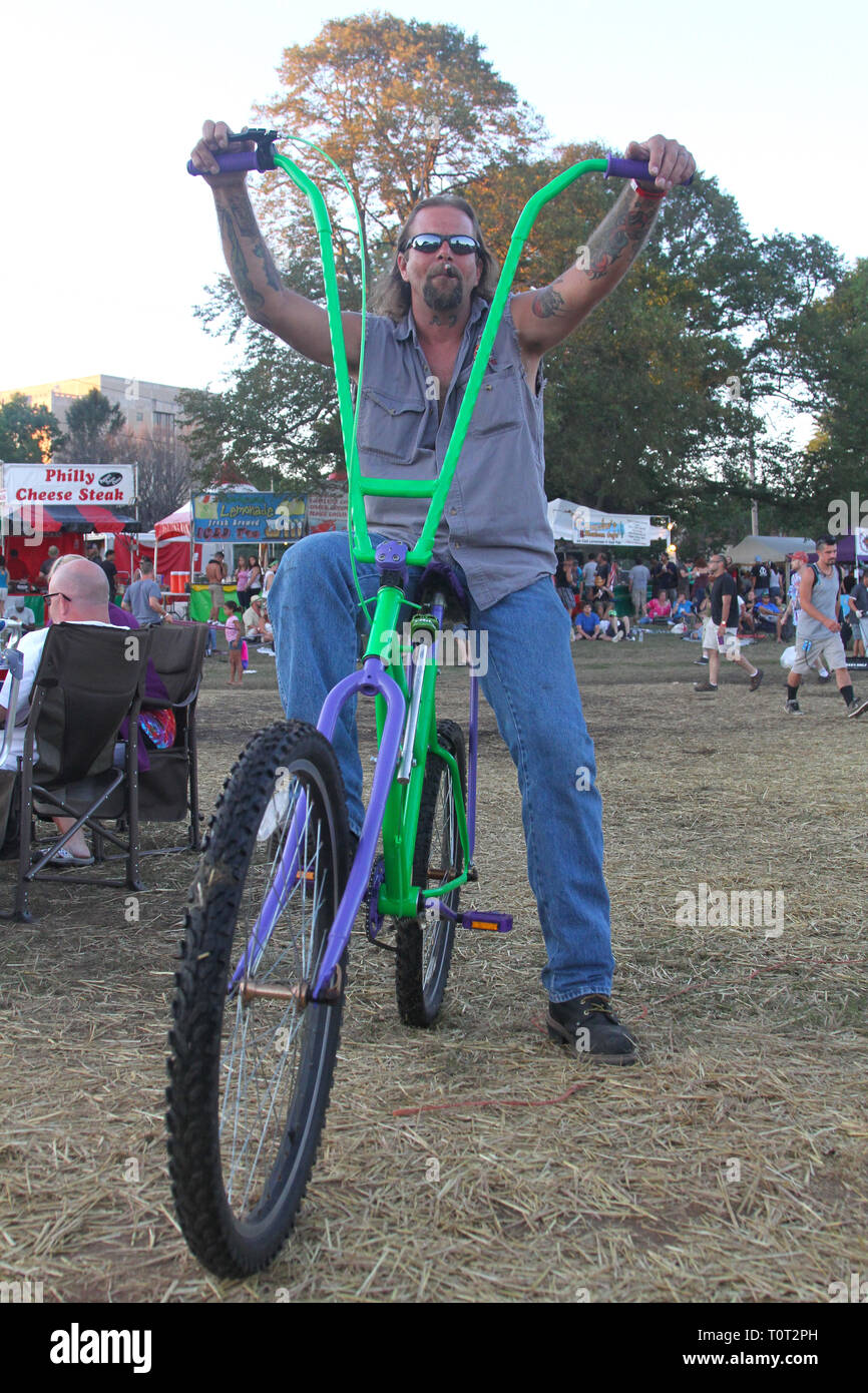 Ce concert goer est illustré posant pour l'appareil photo sur son vélo du broyeur à un festival de musique en plein air. Banque D'Images