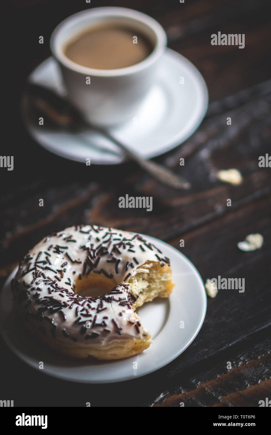 Une bouchée donut blanc avec du chocolat et parsemer de tasse de café sur la table en bois Banque D'Images