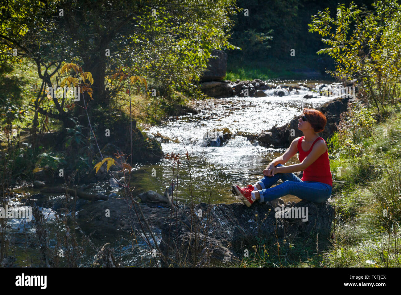 Jeune femme assise sur une pierre près d'un petit ruisseau sur une chaude journée d'automne Banque D'Images