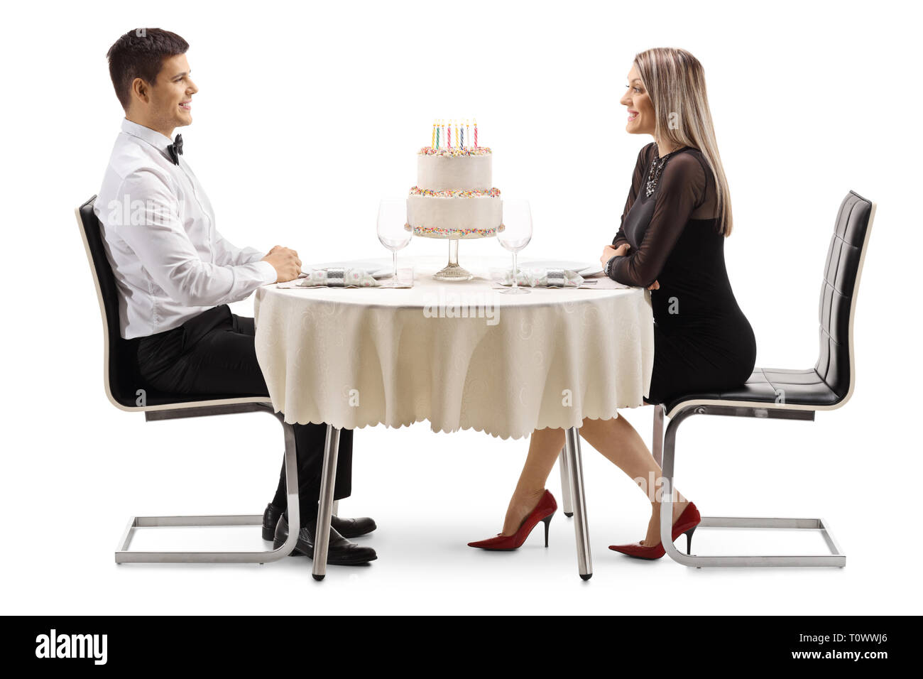 Profil tourné sur toute la longueur d'un jeune homme et femme fêter un anniversaire dans un restaurant avec un gâteau sur une table isolé sur fond blanc Banque D'Images