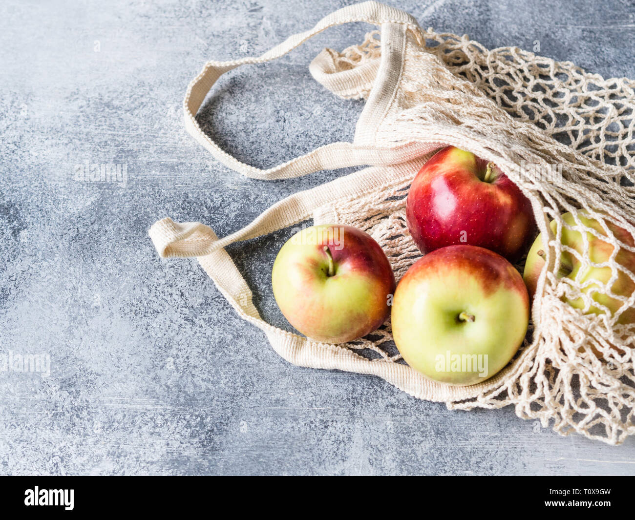 Eco-friendly beige Panier à pommes rouges sur fond gris. Sac de chaîne avec des fruits. Zéro déchets en plastique, pas de concept. Banque D'Images