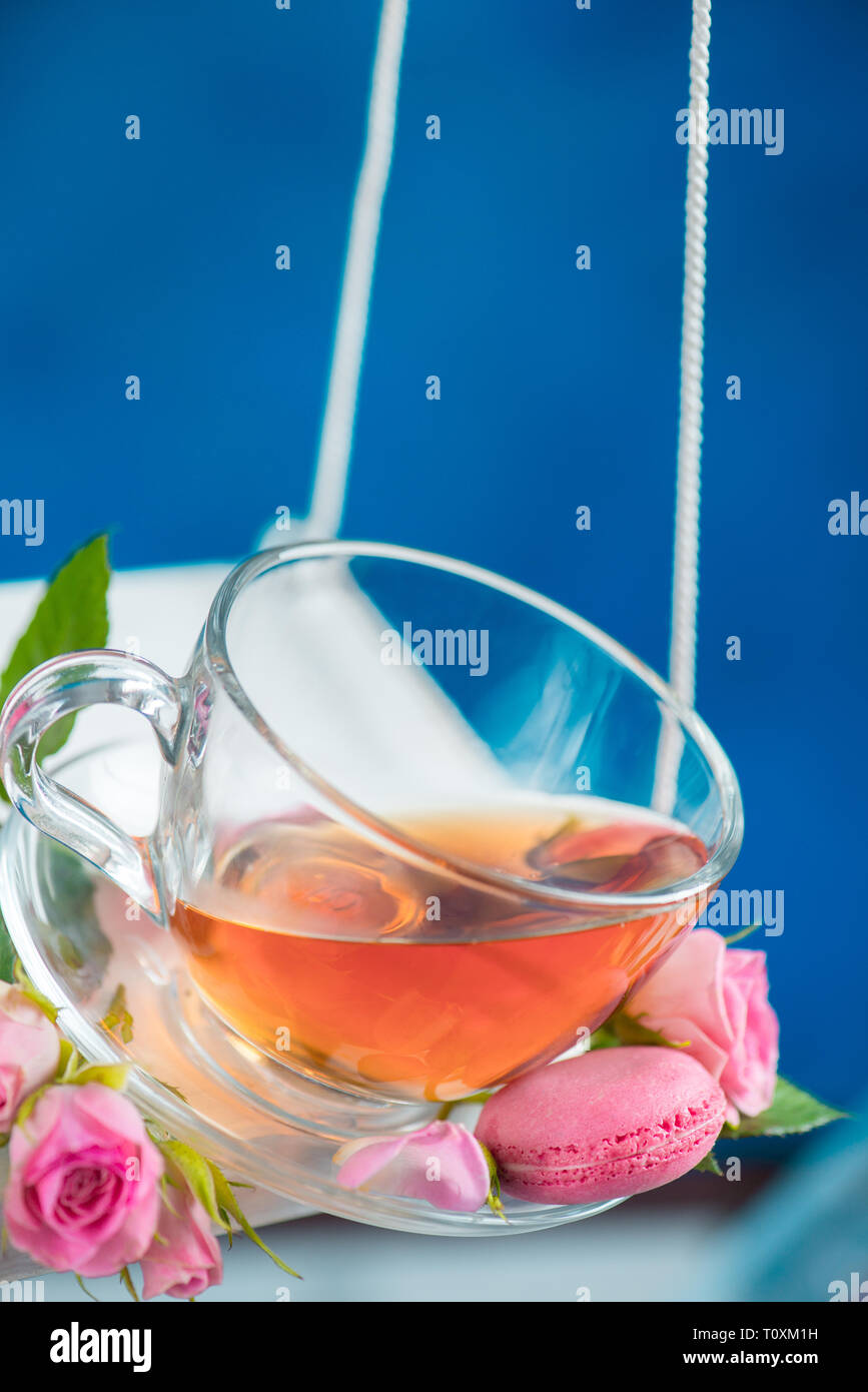 Balançoires en mouvement avec rose thé, macaron cookies, et des fleurs roses sur le concept de l'énergie ressort sur un fond bleu vif Banque D'Images