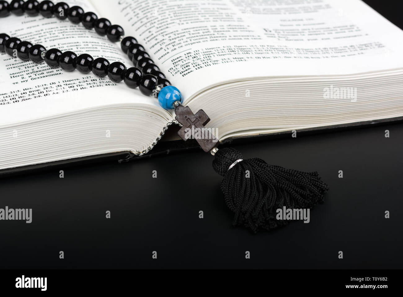 Libre d'ouverte Sainte Bible et chapelet avec croix sur fond noir. Concept de la religion. Texte cyrillique. Banque D'Images