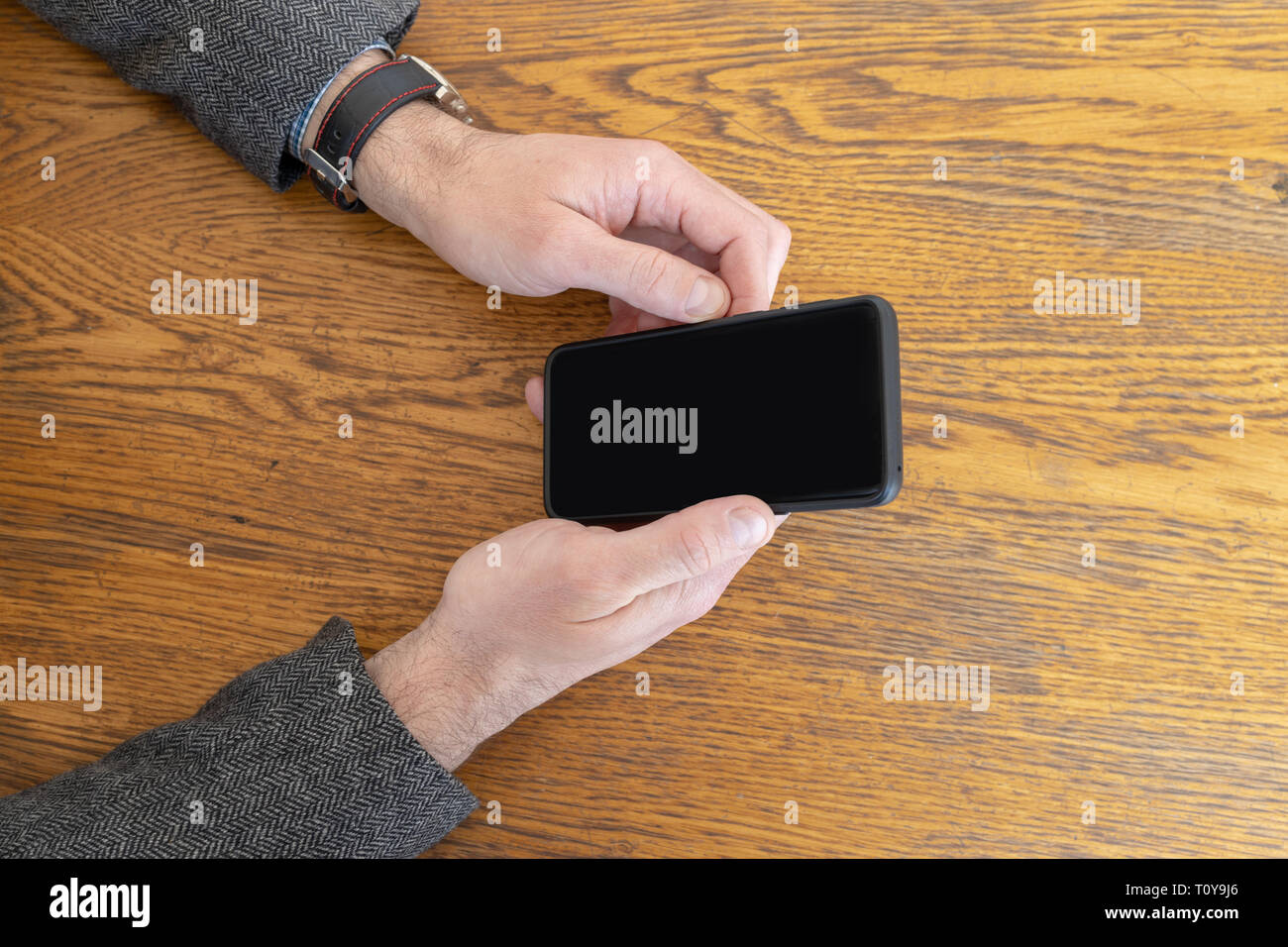 Homme tenant un téléphone intelligent dans les mains en attendant d'être servis au restaurant. Téléphone avec écran incurvé noir vide Banque D'Images