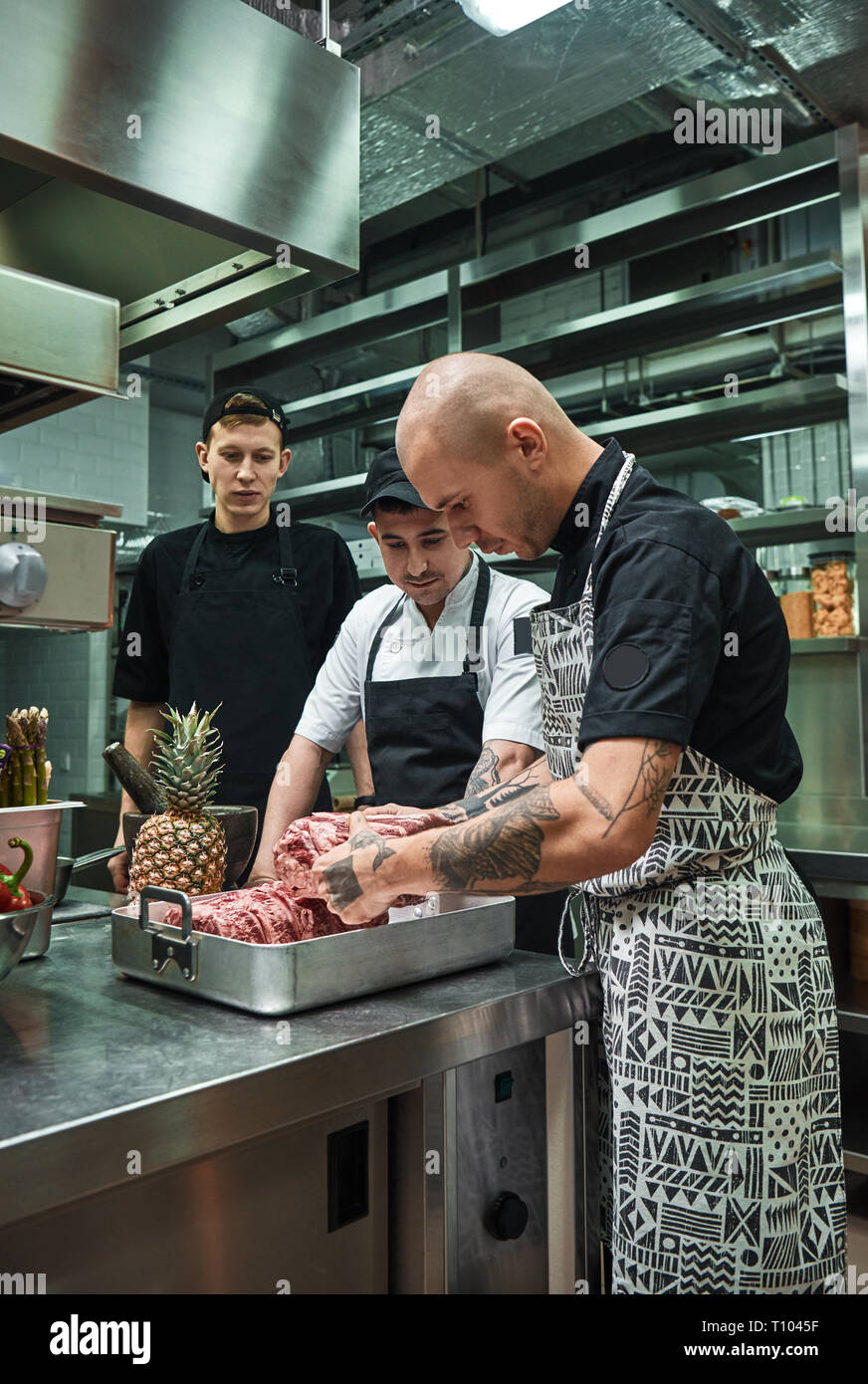 L'école culinaire. Chef professionnel avec des tatouages sur ses mains tenant une viande rouge et les auxiliaires d'enseignement comment choisir la droite. La préparation des aliments Banque D'Images