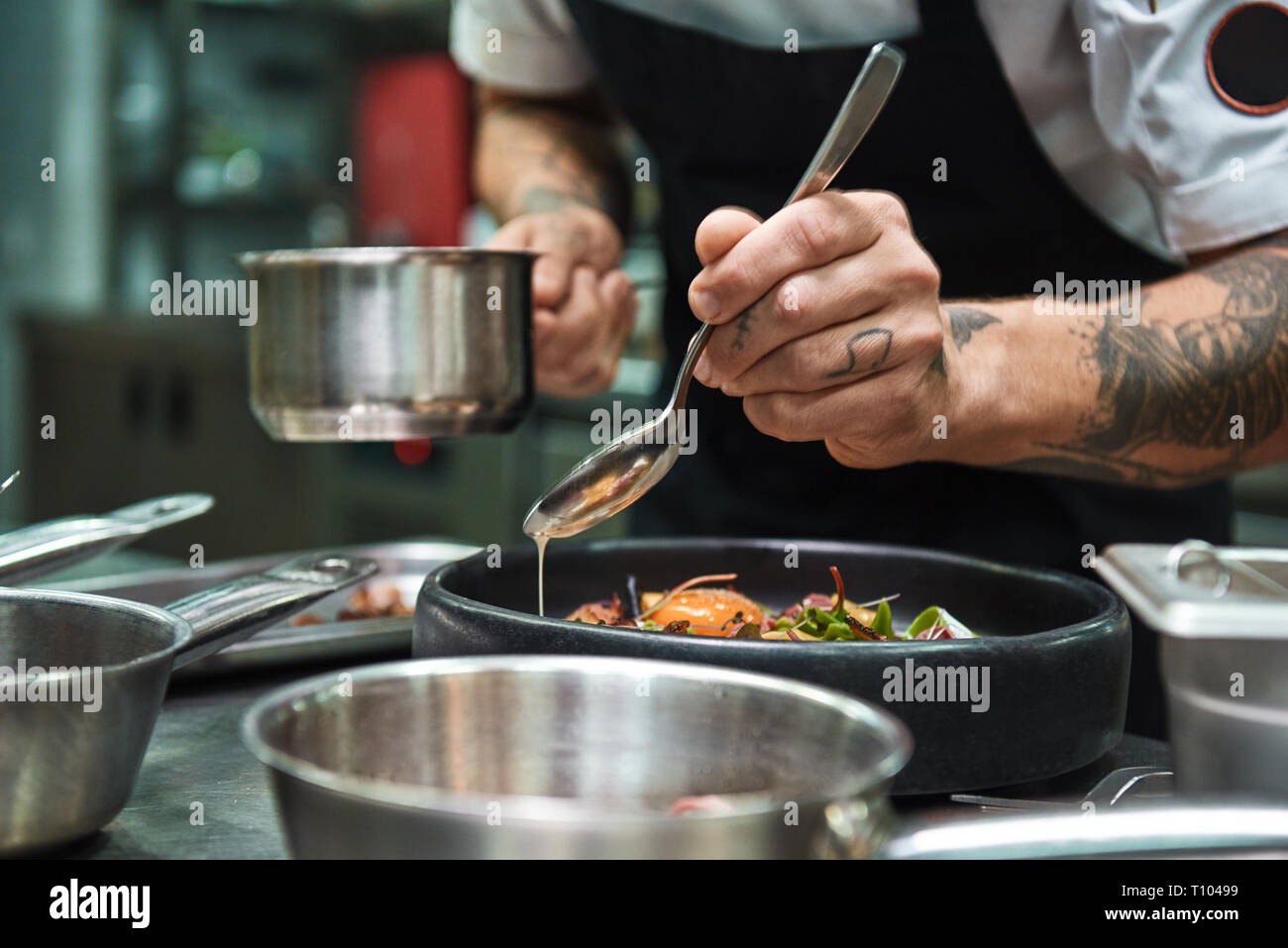 Recette secrète. La photo en gros du chef les mains avec plusieurs tatouages ajouter la sauce pour pâtes italiennes Carbonara. Concept alimentaire Banque D'Images