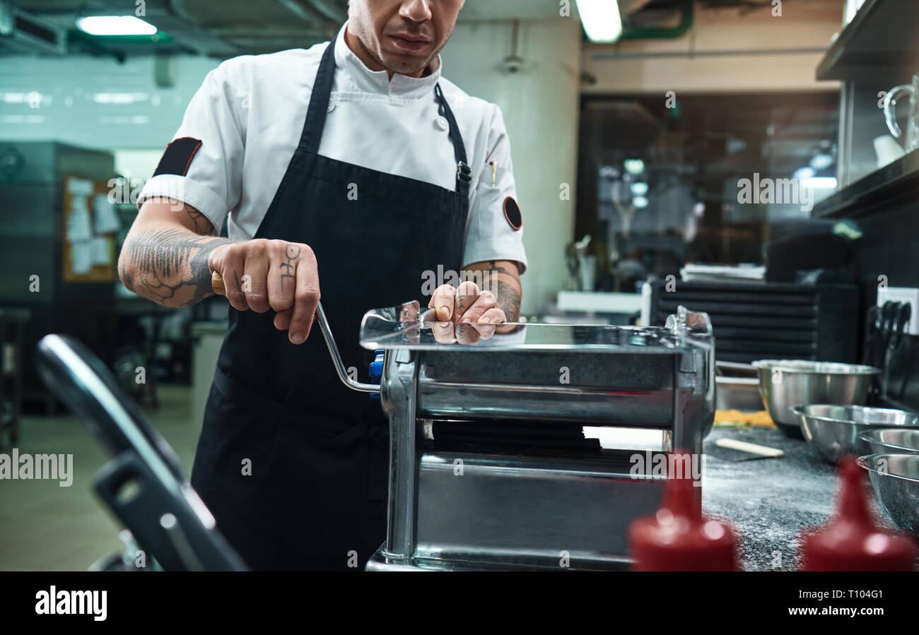 J'adore la cuisine italienne, Portrait de chef professionnel rouler une pâte noire par machine à pâtes dans la cuisine du restaurant. Cuisson Banque D'Images