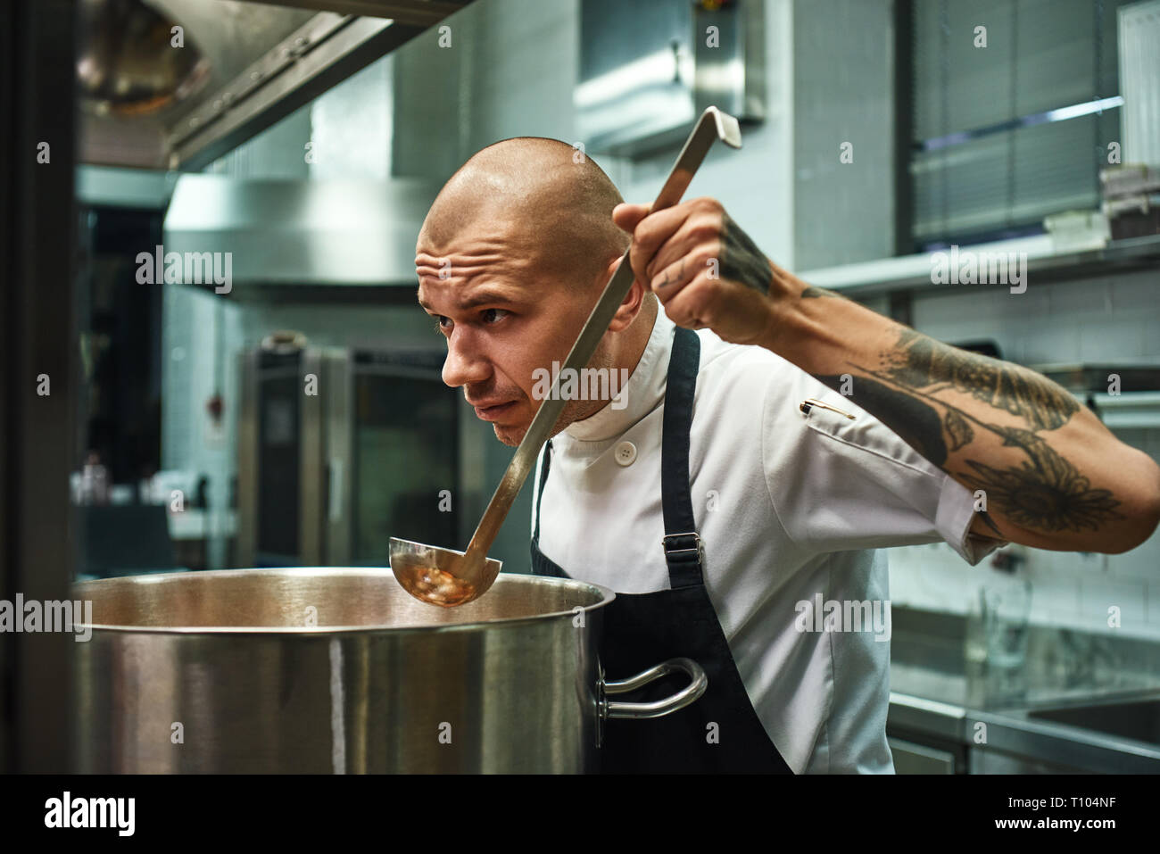 L'odorat si bon jeune et beau chef avec des tatouages sur ses bras et sentir une dégustation de soupe dans un restaurant de cuisine. Concept de cuisine Banque D'Images