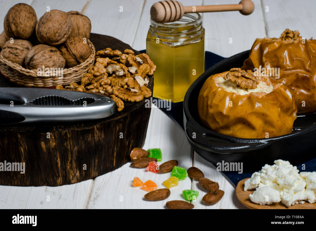 Pommes au four avec du fromage cottage et les écrous se trouvent dans un plat de cuisson noir sur une table en bois blanc, à côté d'un pot de miel et une planche en bois sur laquelle l'écrous Banque D'Images