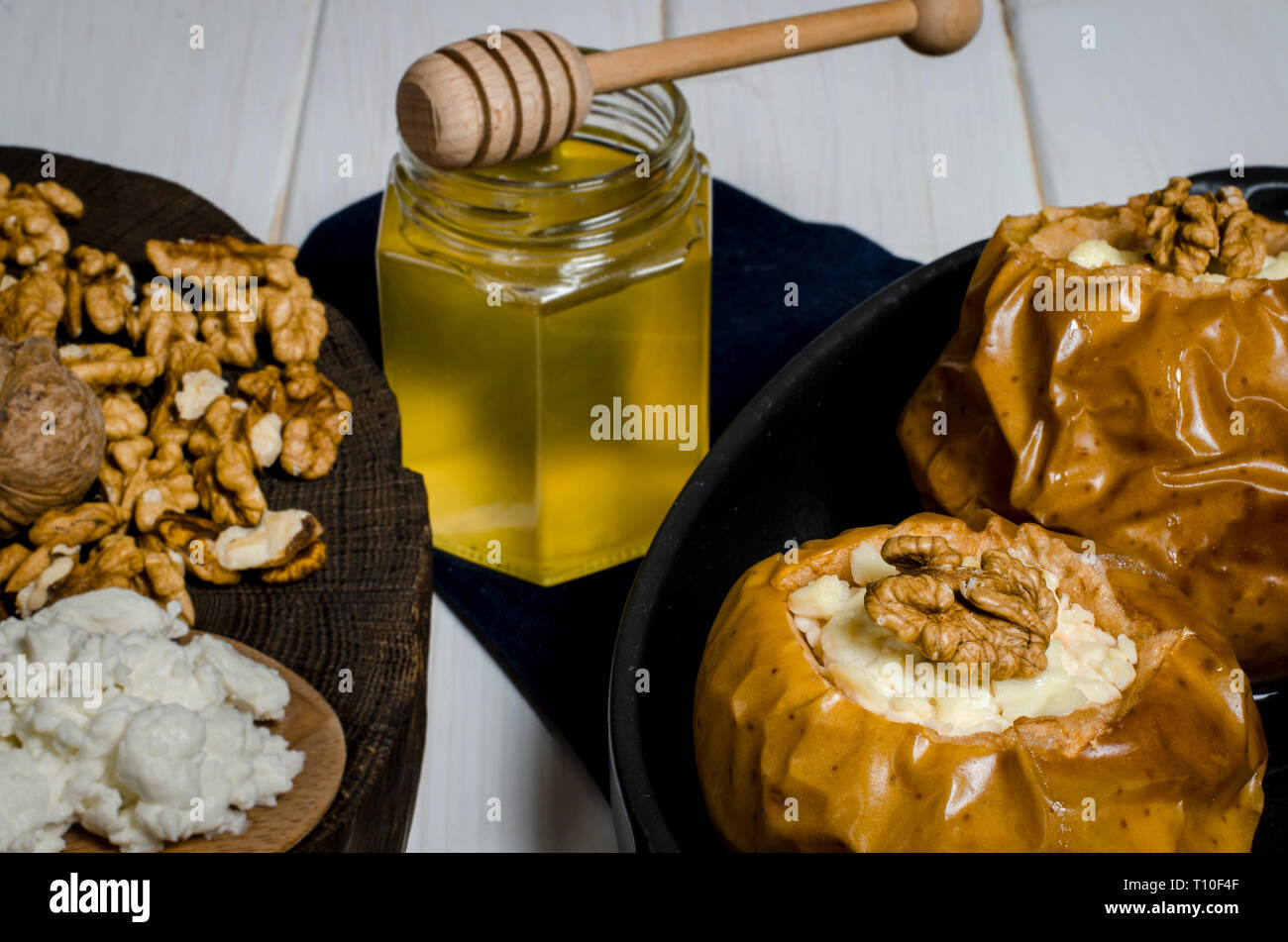 Pommes au four avec du fromage cottage et les écrous se trouvent dans un plat de cuisson noir sur une table en bois blanc, à côté d'un pot de miel et une planche en bois sur laquelle l'écrous Banque D'Images