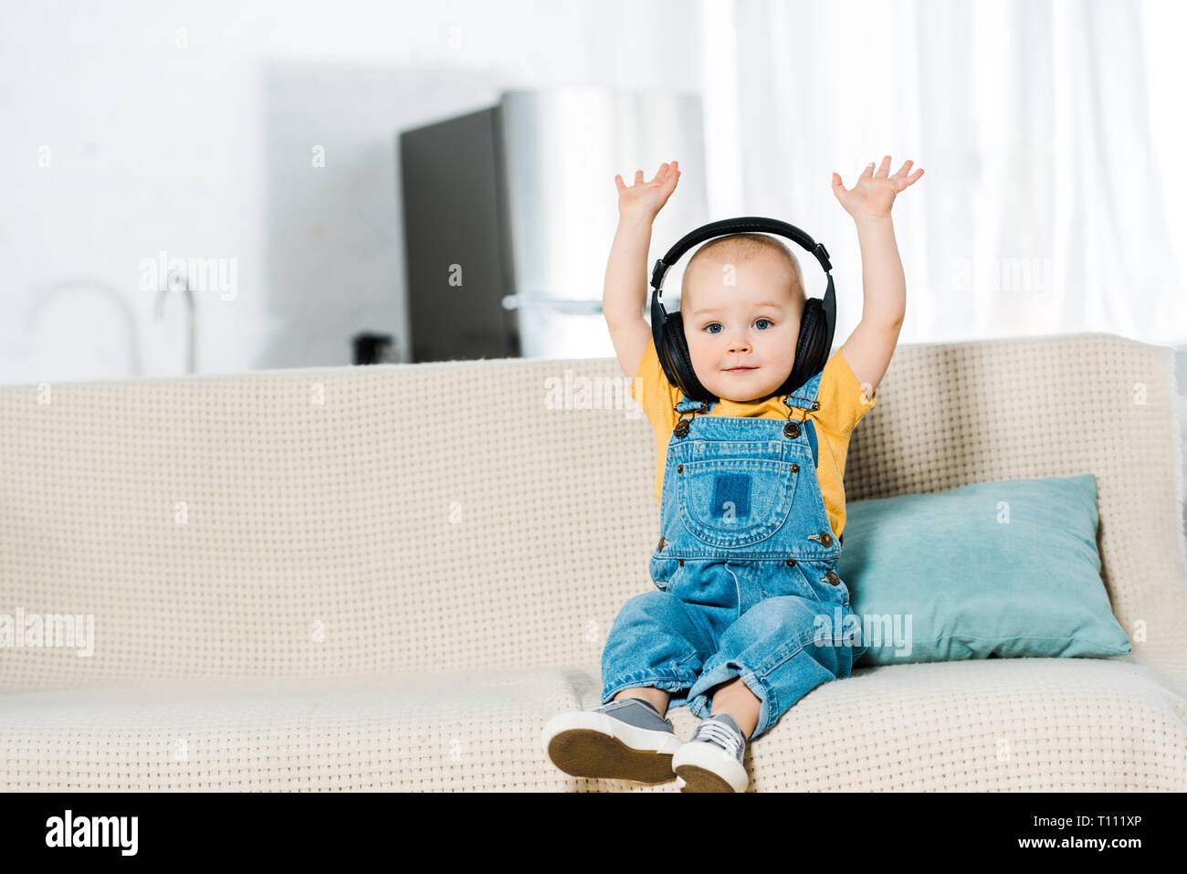 Adorable bébé de sexe masculin dans les écouteurs avec les mains dans l'air à la caméra et à l'écoute de la musique à la maison Banque D'Images