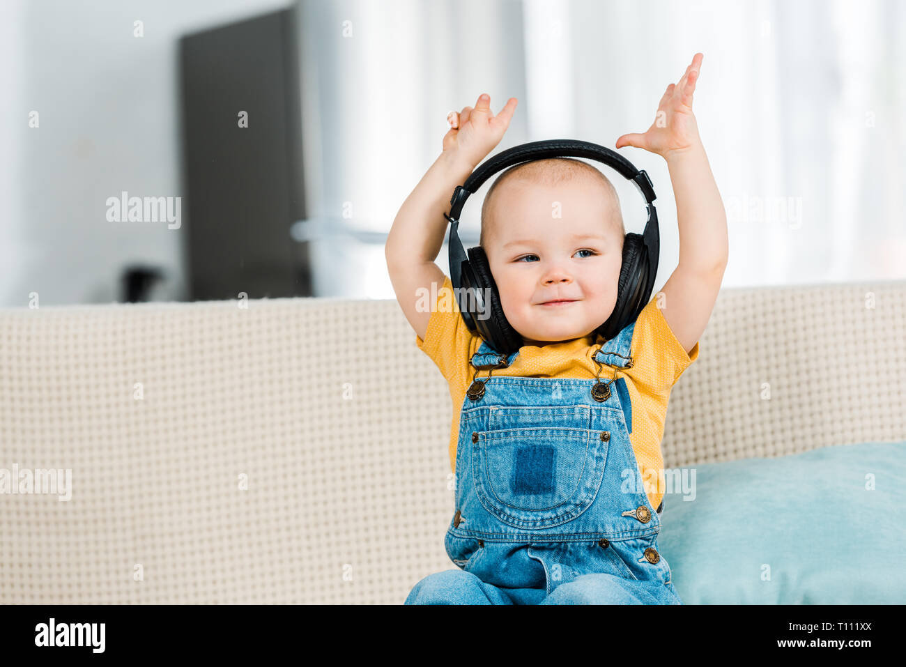 Adorable bébé de sexe masculin dans les écouteurs avec les mains dans l'air d'écouter la musique à la maison Banque D'Images