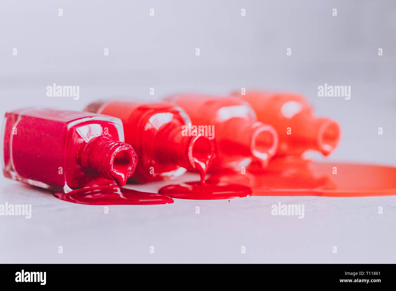 Bouteilles de vernis à ongles dans différentes nuances de rouge à l'orange et violet couleur déversant sur la surface en bois, concept de l'industrie cosmétique et manucure Banque D'Images