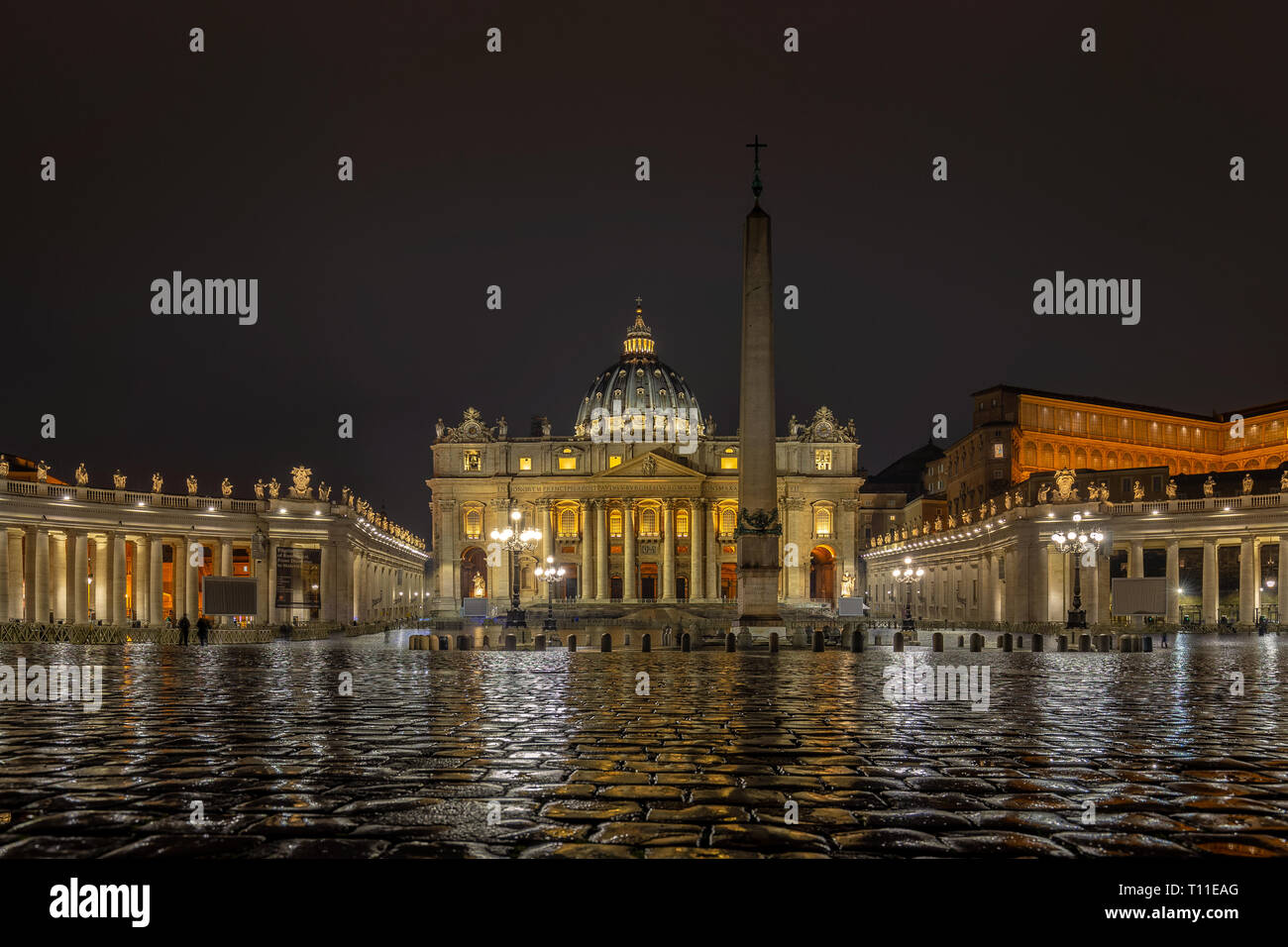 La Basilique St Pierre du cœur de la Cité du Vatican. Une chaussée mouillée reflète les lumières de l'église et de Bernini columnade Banque D'Images