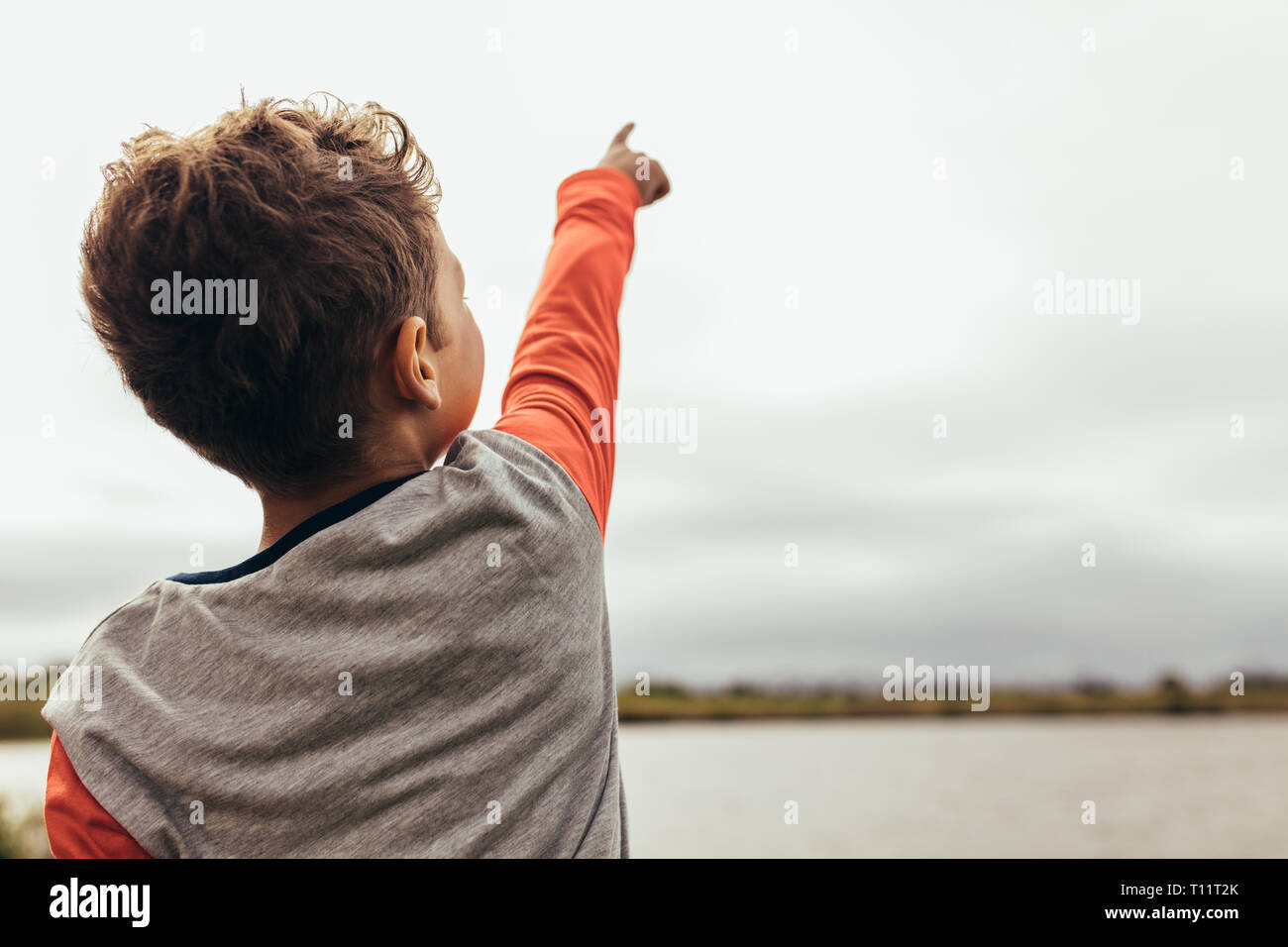 Vue arrière d'un enfant debout près du lac et montrant quelque chose à quelqu'un. Close up vue arrière d'un garçon pointant son doigt vers le ciel. Banque D'Images